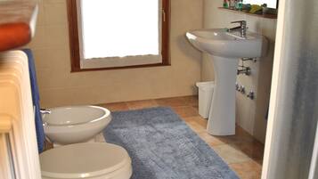 Un baño con inodoro, bidé, lavamanos y ventana.