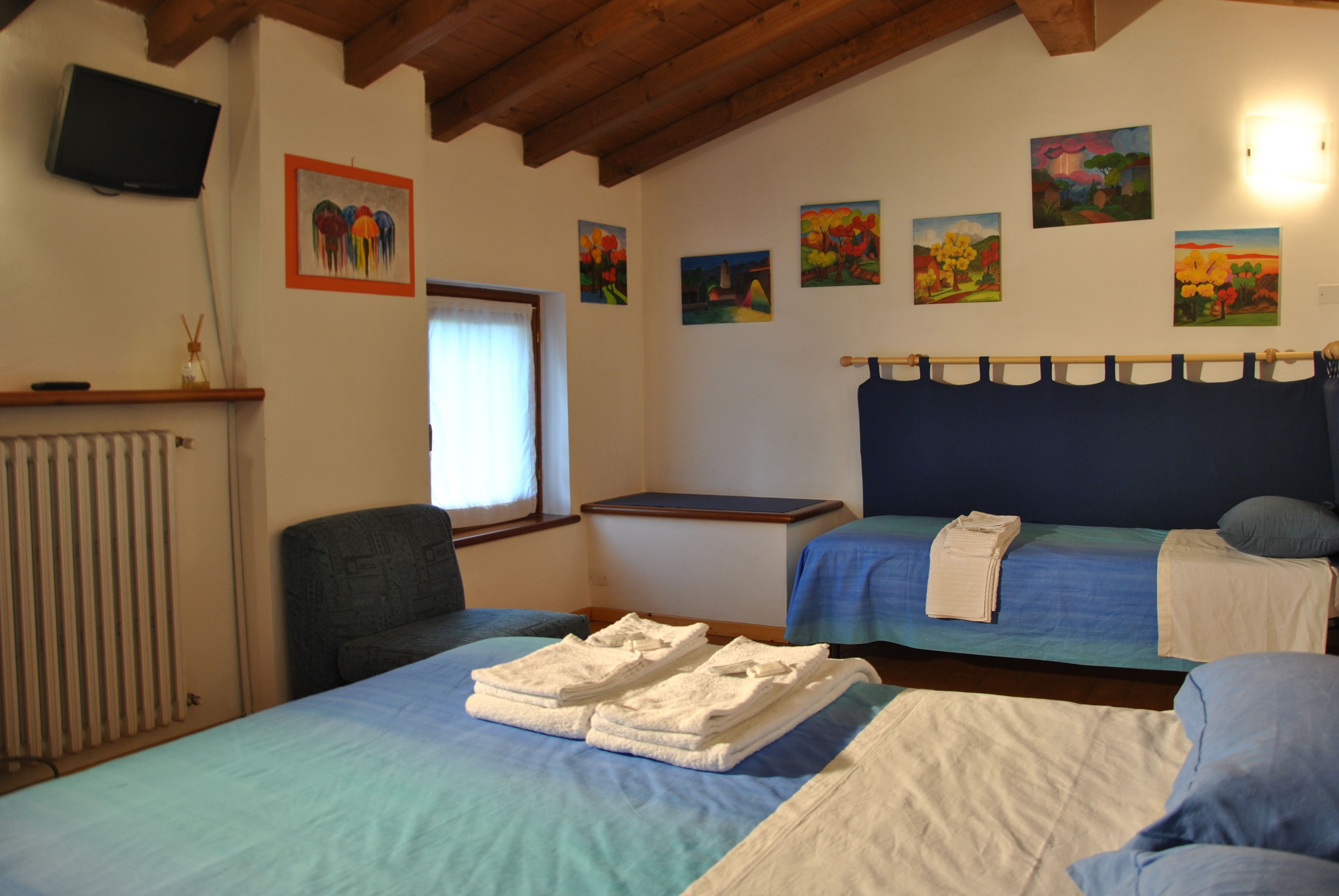 Una habitación con dos camas, una silla, un radiador y obras de arte en las paredes.