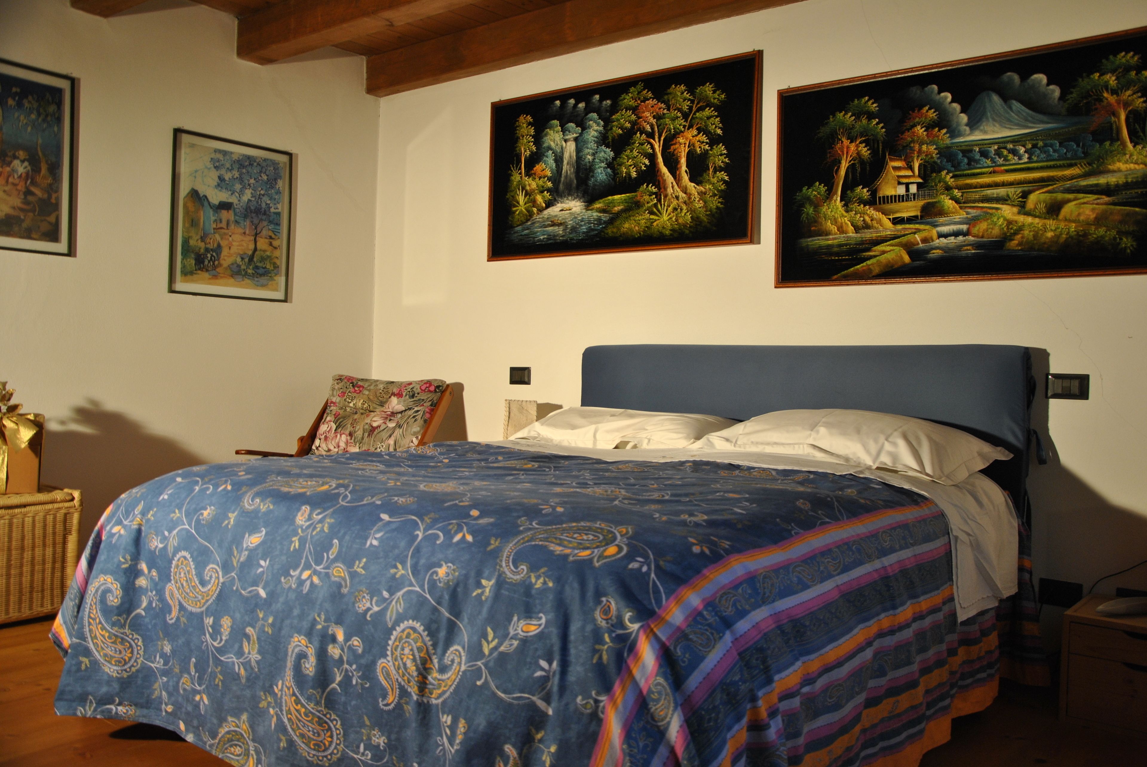 Een slaapkamer met een groot bed, een nachtkastje, een stoel en drie schilderijen aan de muur.