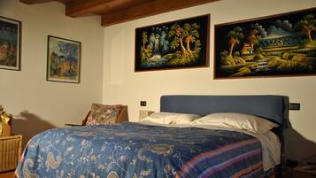 Een slaapkamer met een groot bed, een nachtkastje, een stoel en drie schilderijen aan de muur.