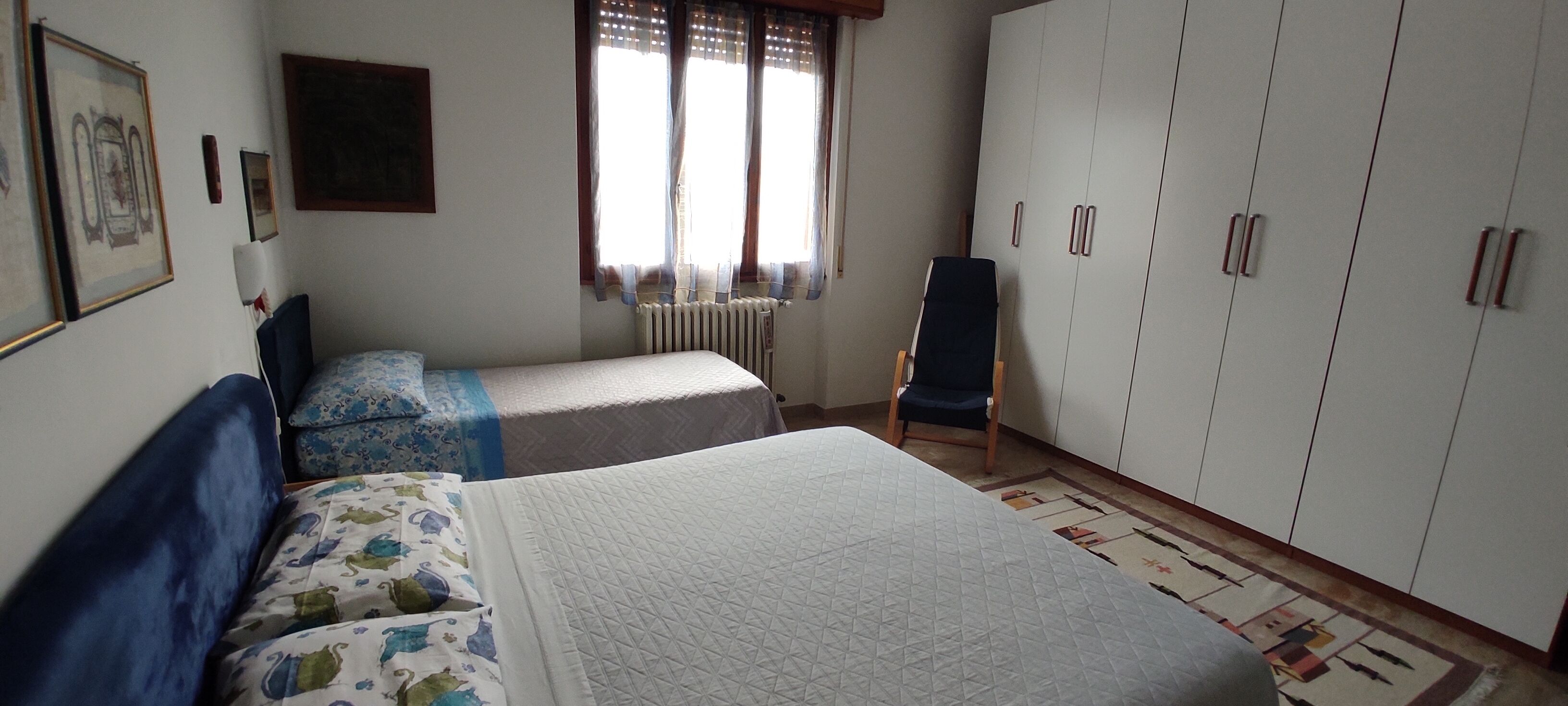 A bedroom with two beds, a chair, a wardrobe, and a radiator.