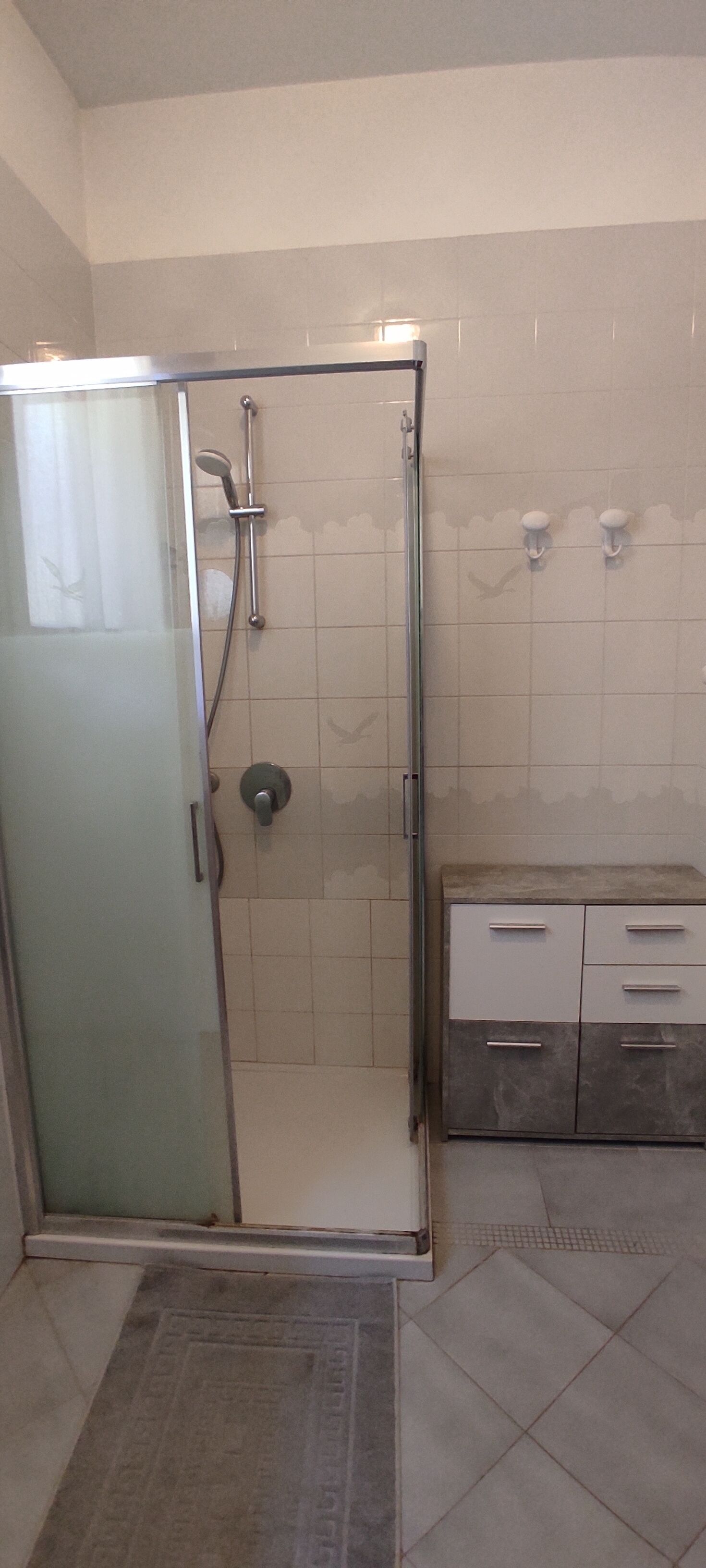 Un baño con cabina de ducha de vidrio, tocador con cajones y suelo de baldosas.