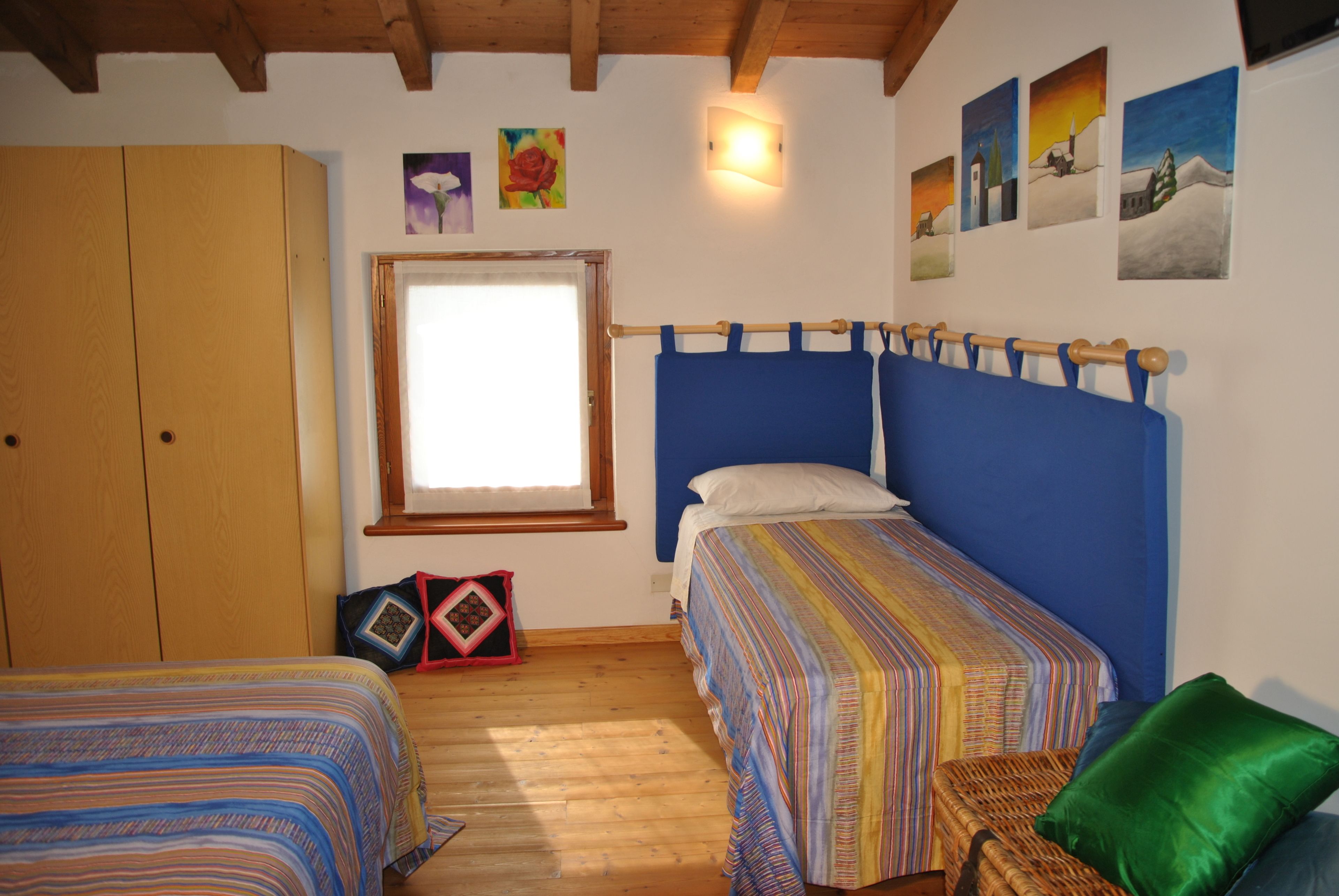 Ein Schlafzimmer mit zwei Einzelbetten, Holzboden, einem Kleiderschrank, einem Fenster und Wandbildern.