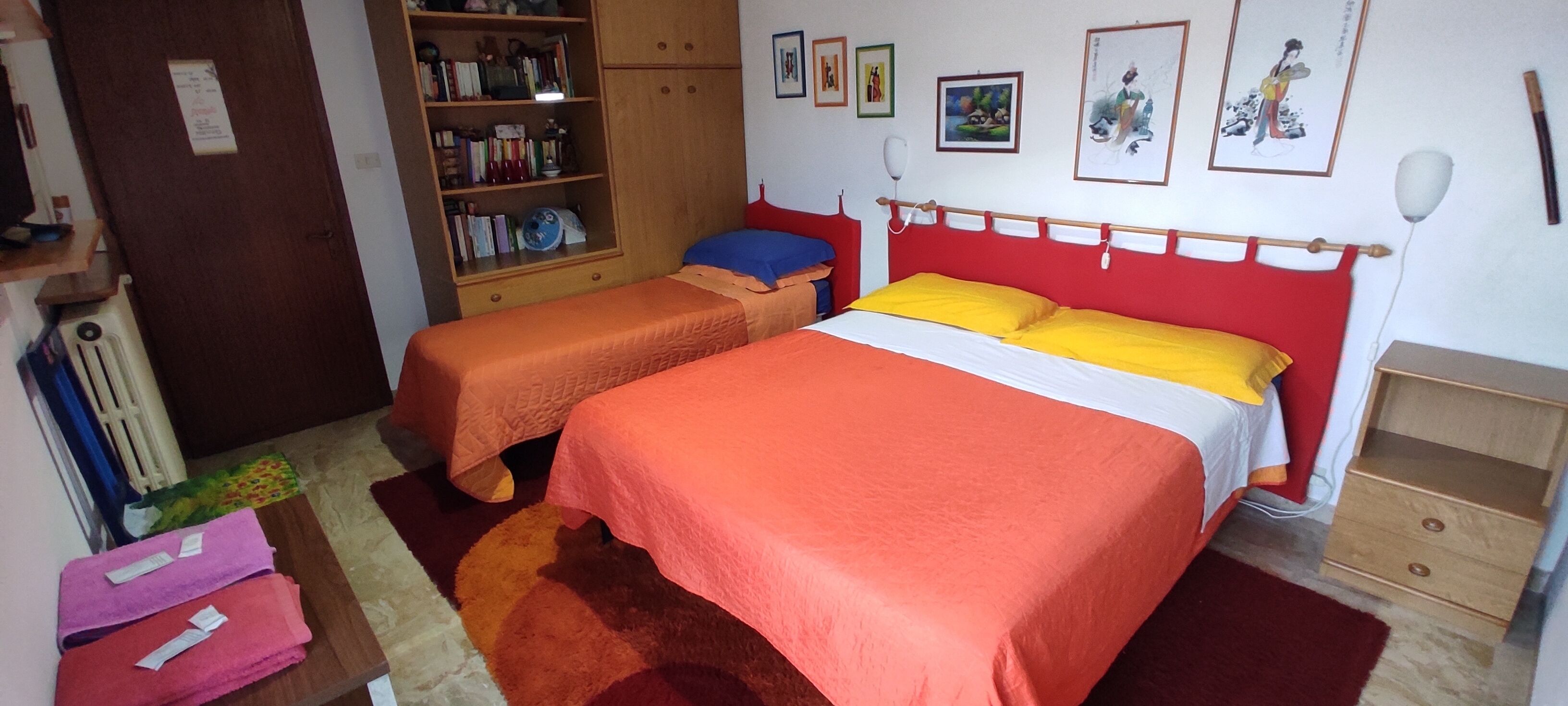 Ein Schlafzimmer mit zwei Betten, einem Holzschrank, einem Bücherregal und einem roten Teppich.