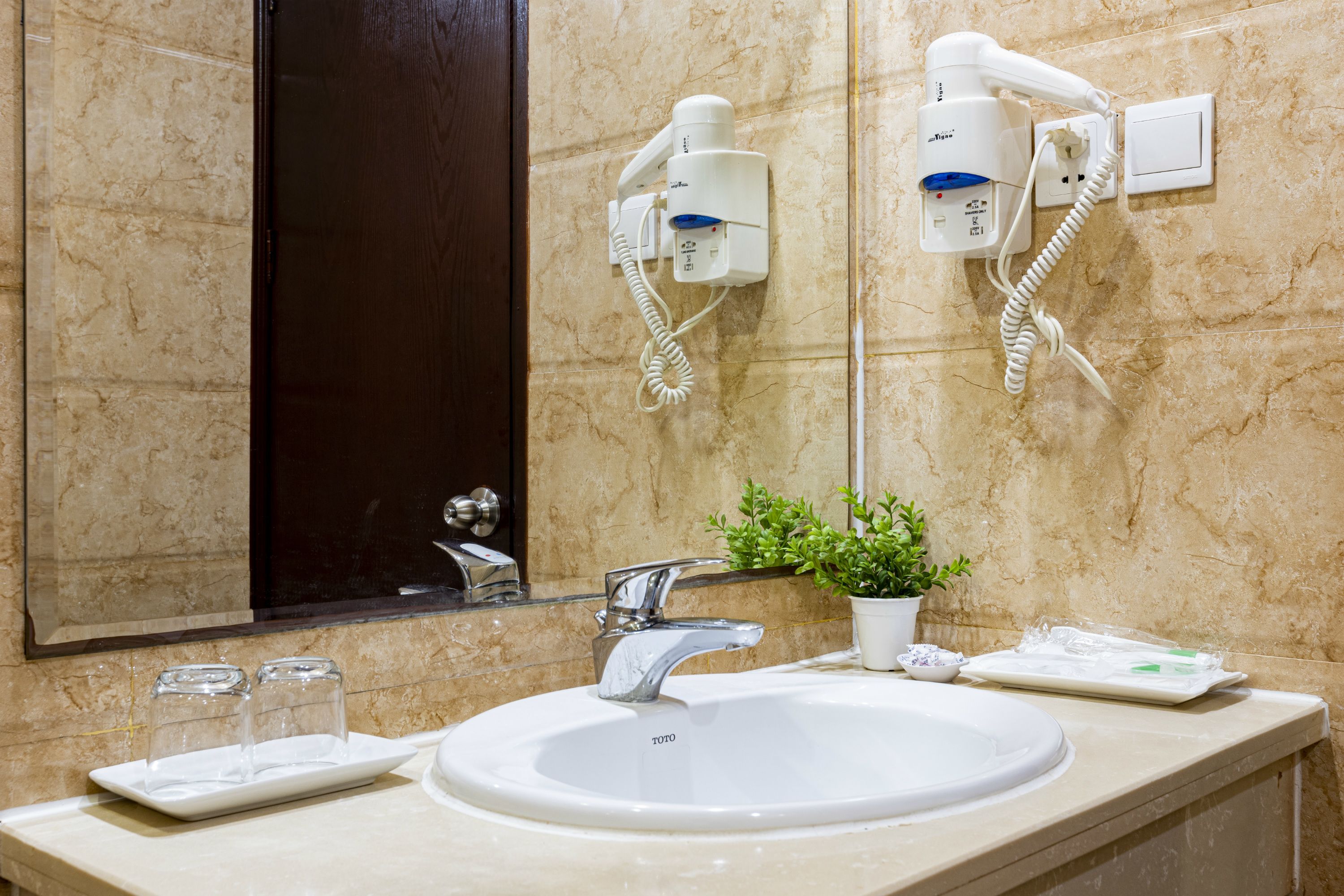 A bathroom with a white sink, a mirror, a hairdryer, and a potted plant.