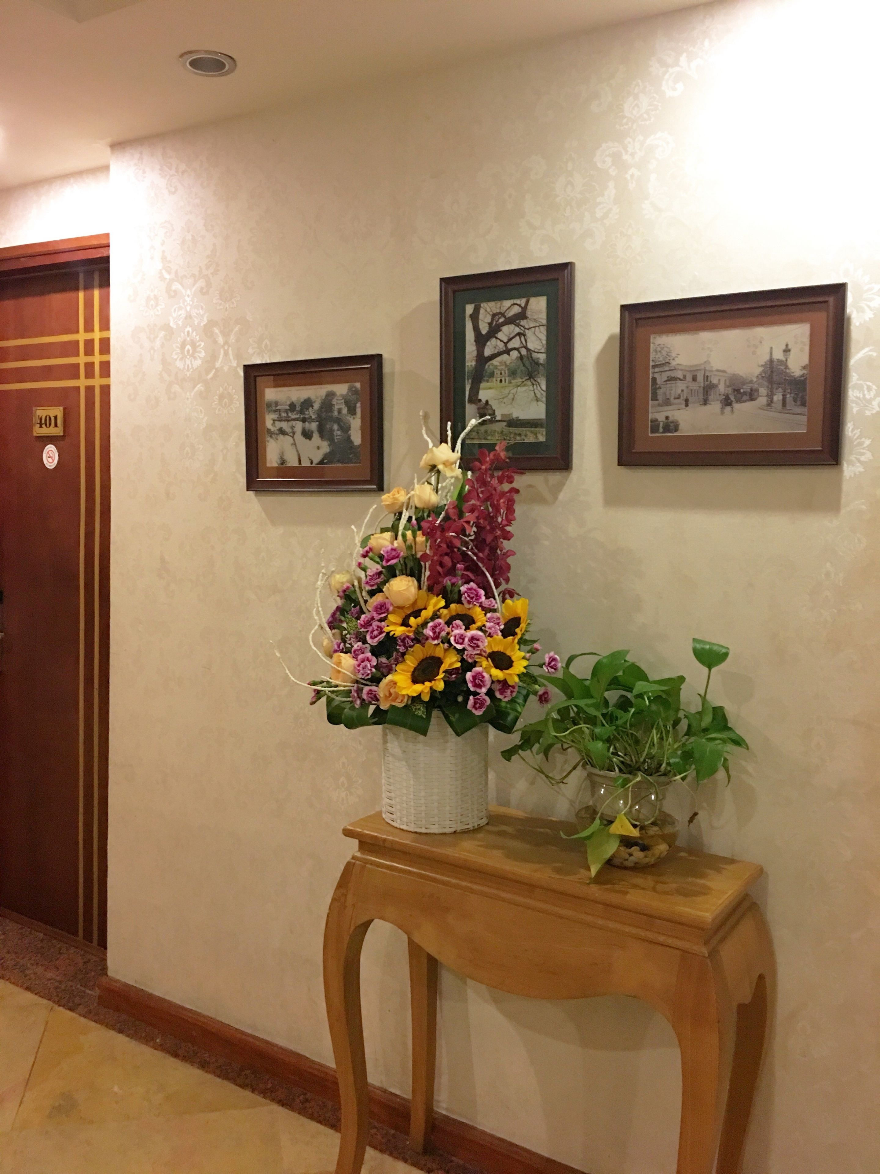 Un pasillo con un banco de madera, un arreglo floral y dos cuadros en la pared.