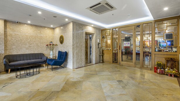A lobby with a marble floor, a sofa, a blue chair, and a wooden cabinet with glass doors. - First Eden Hotel (Hanoi)