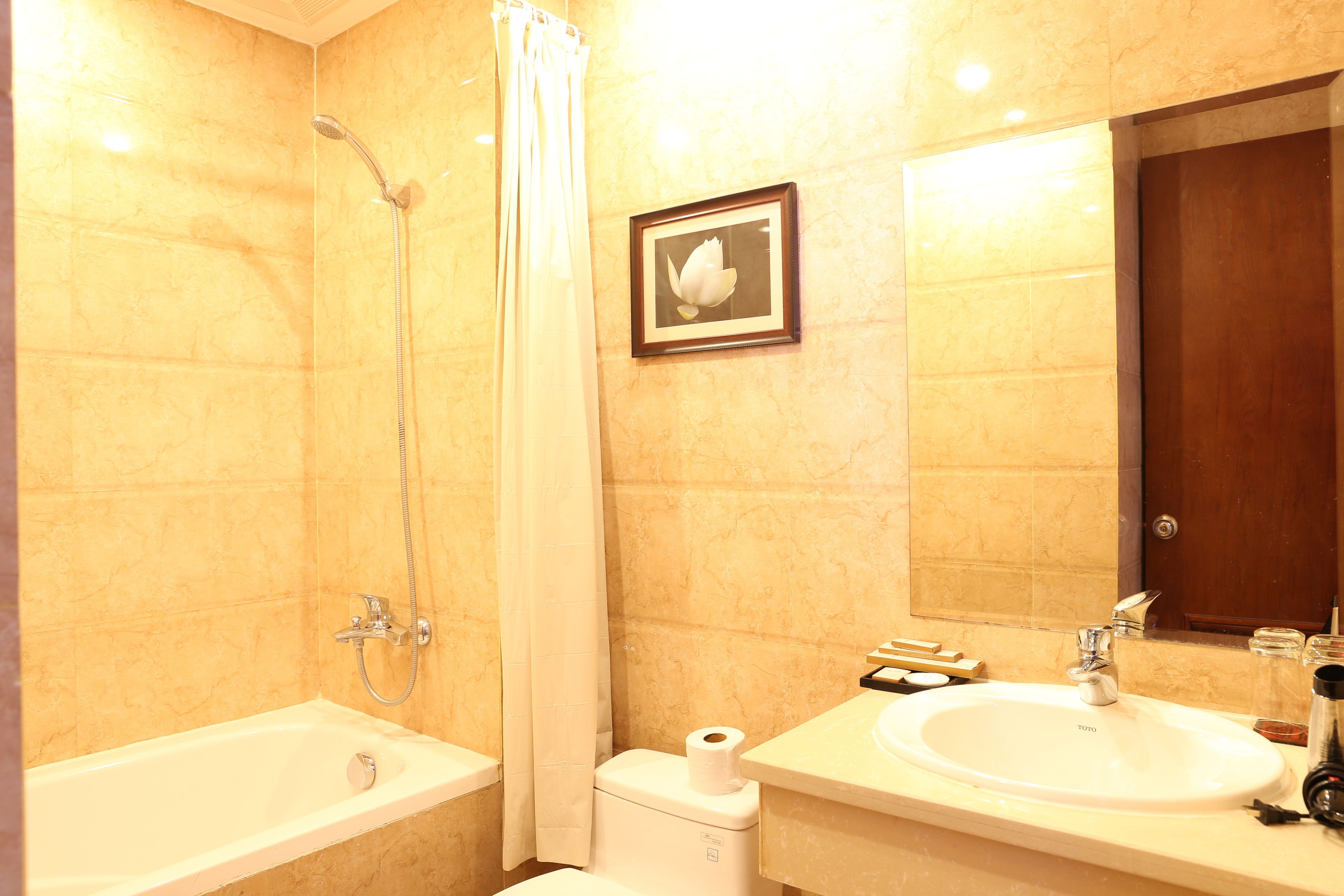 A bathroom with a bathtub, shower, toilet, sink, and a framed picture on the wall.