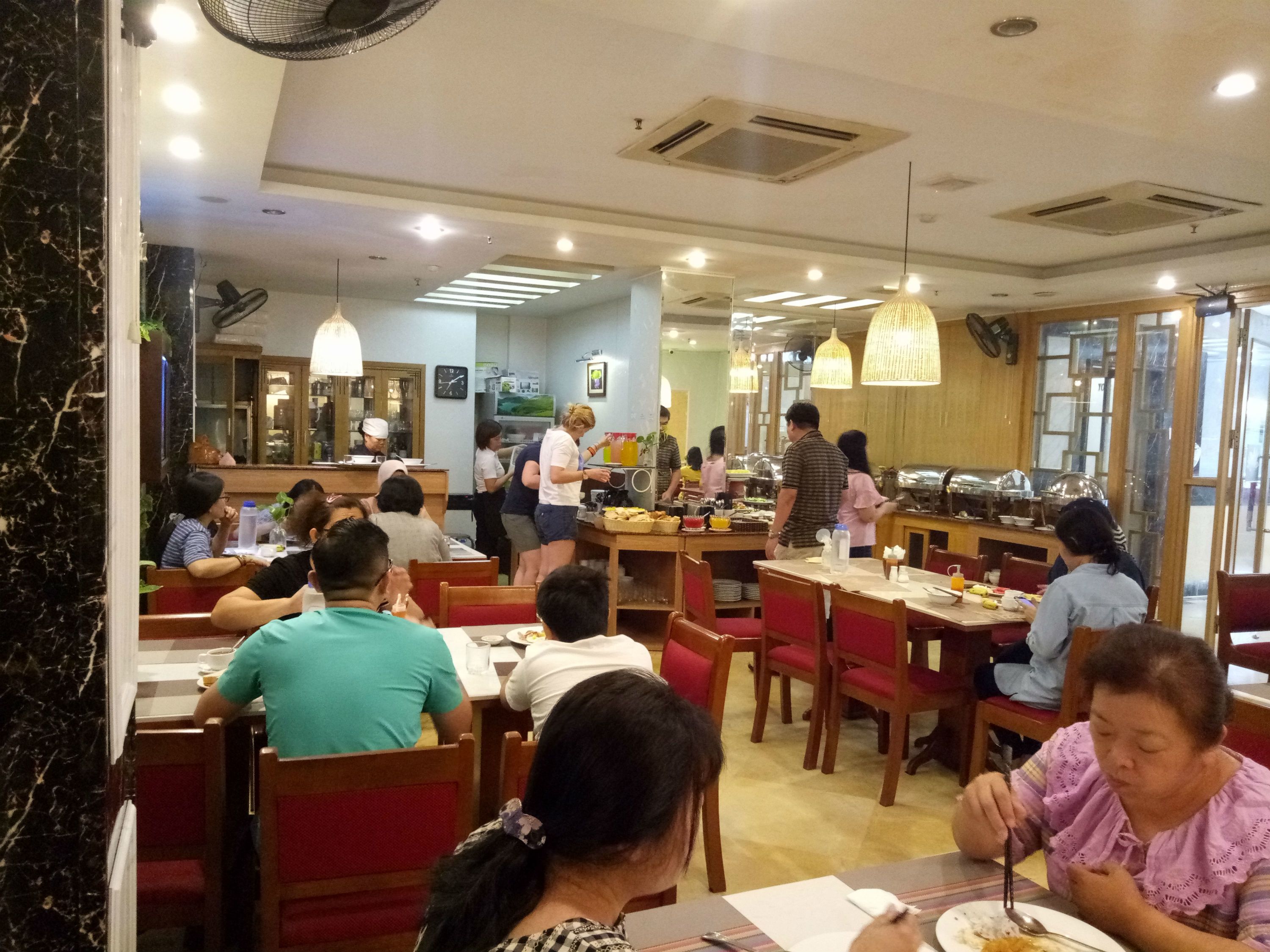 Um restaurante com várias mesas e cadeiras, uma área de buffet e um balcão onde funcionários servem comida.