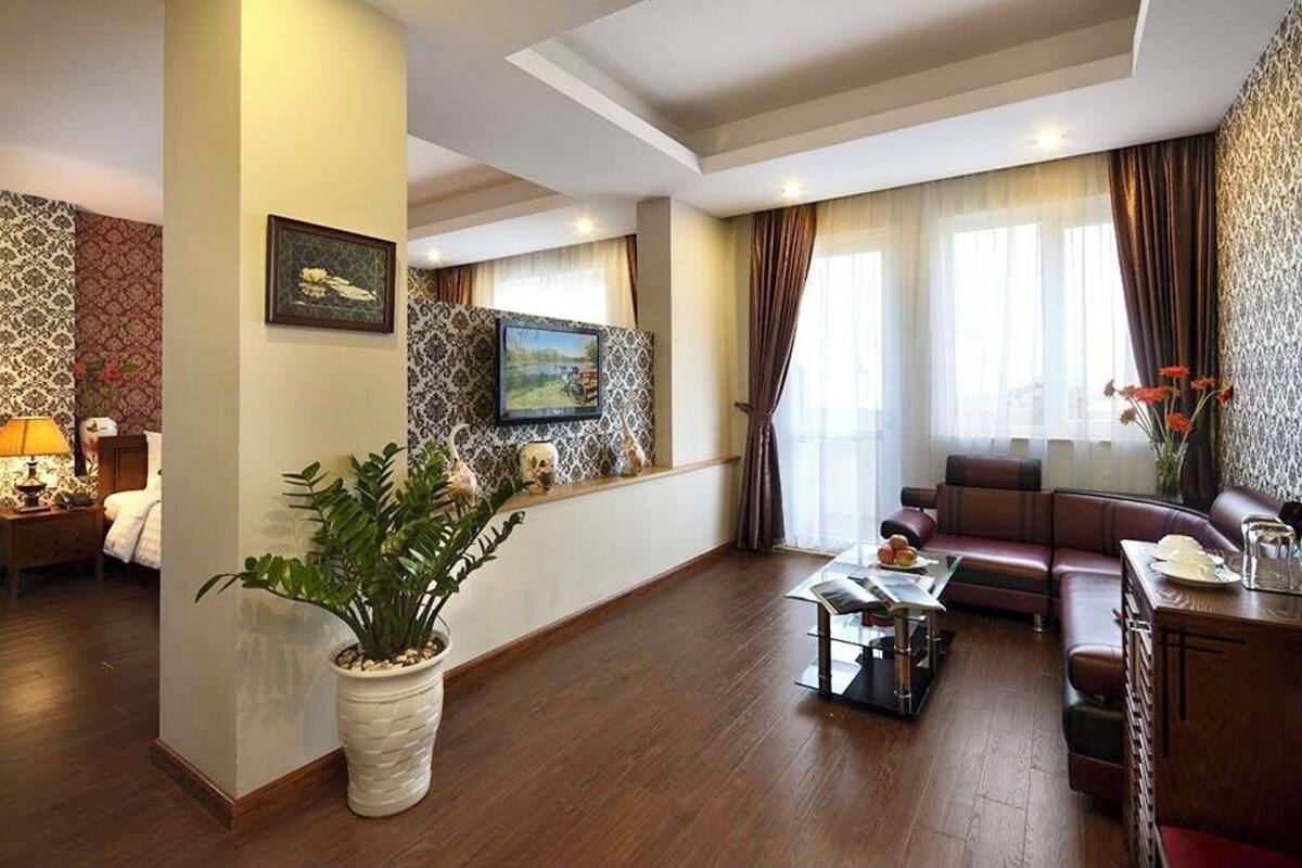 A modern hotel room with a sofa, a dining table, a potted plant, and a painting on the wall.