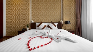A hotel room with a large bed, a nightstand with a lamp, and a wall with patterned wallpaper. - First Eden Hotel (Hanoi)