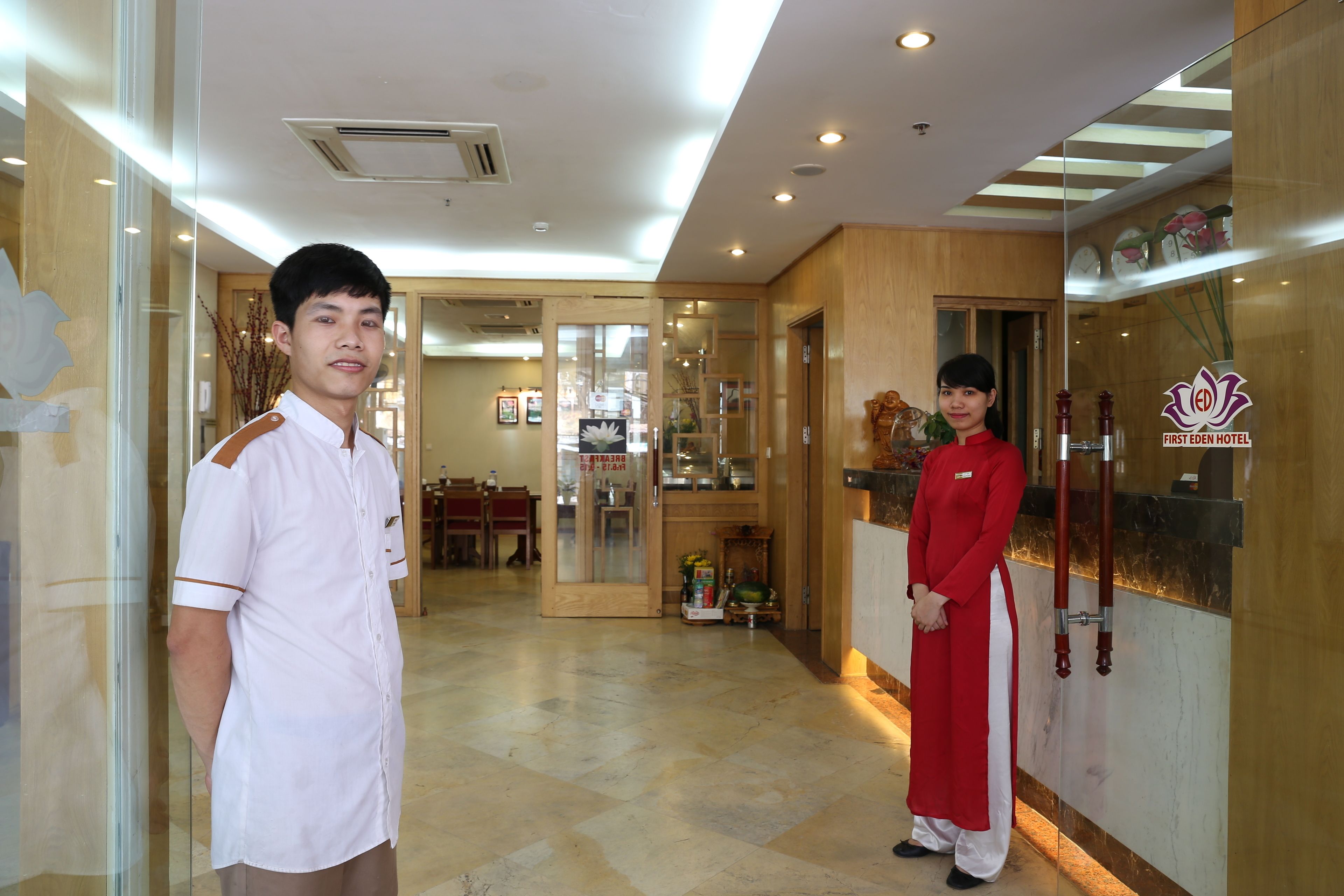 A hotel reception area with a wooden interior, a reception desk, and a glass door leading to the dining area.