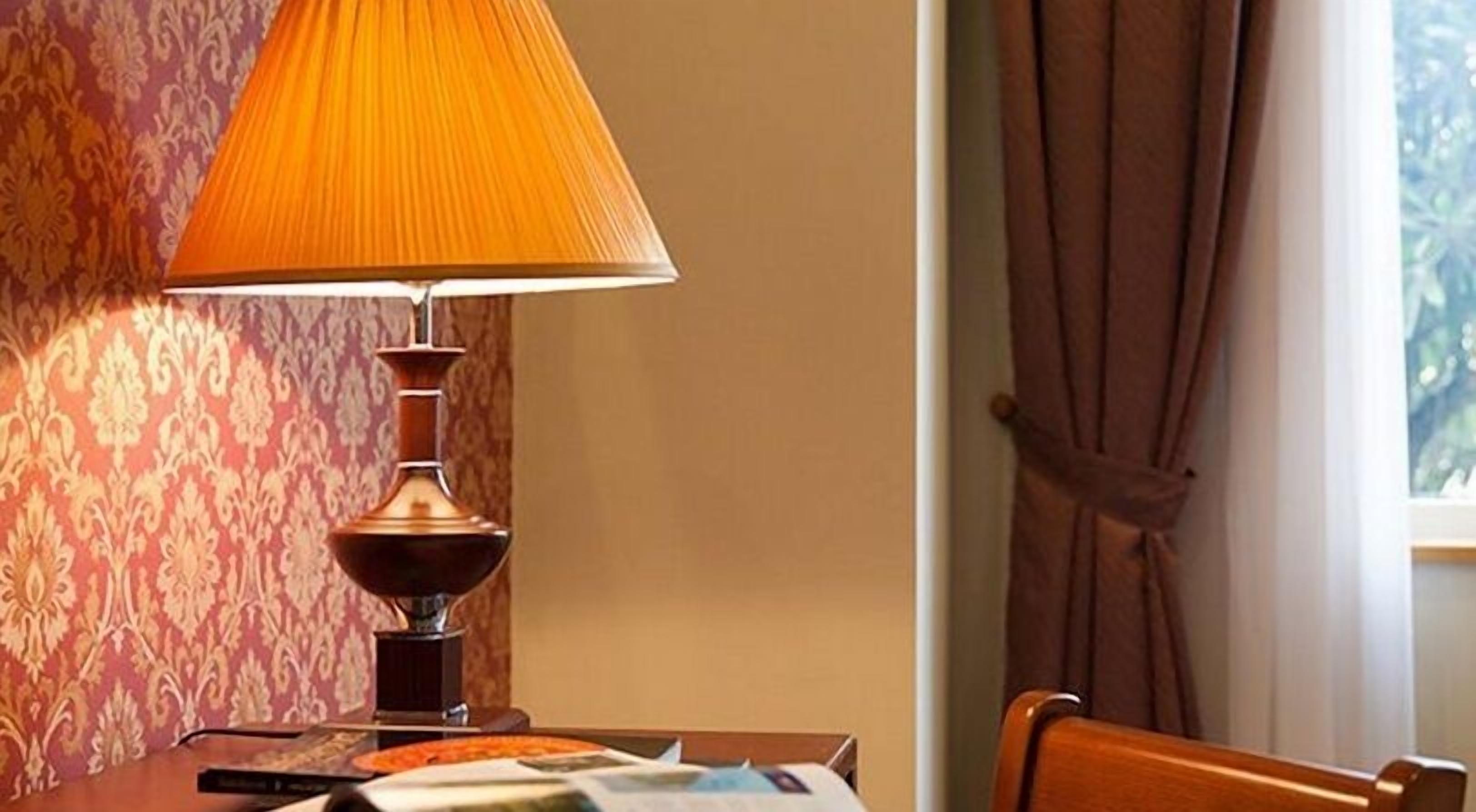A table with a lamp, a pizza, and some papers.