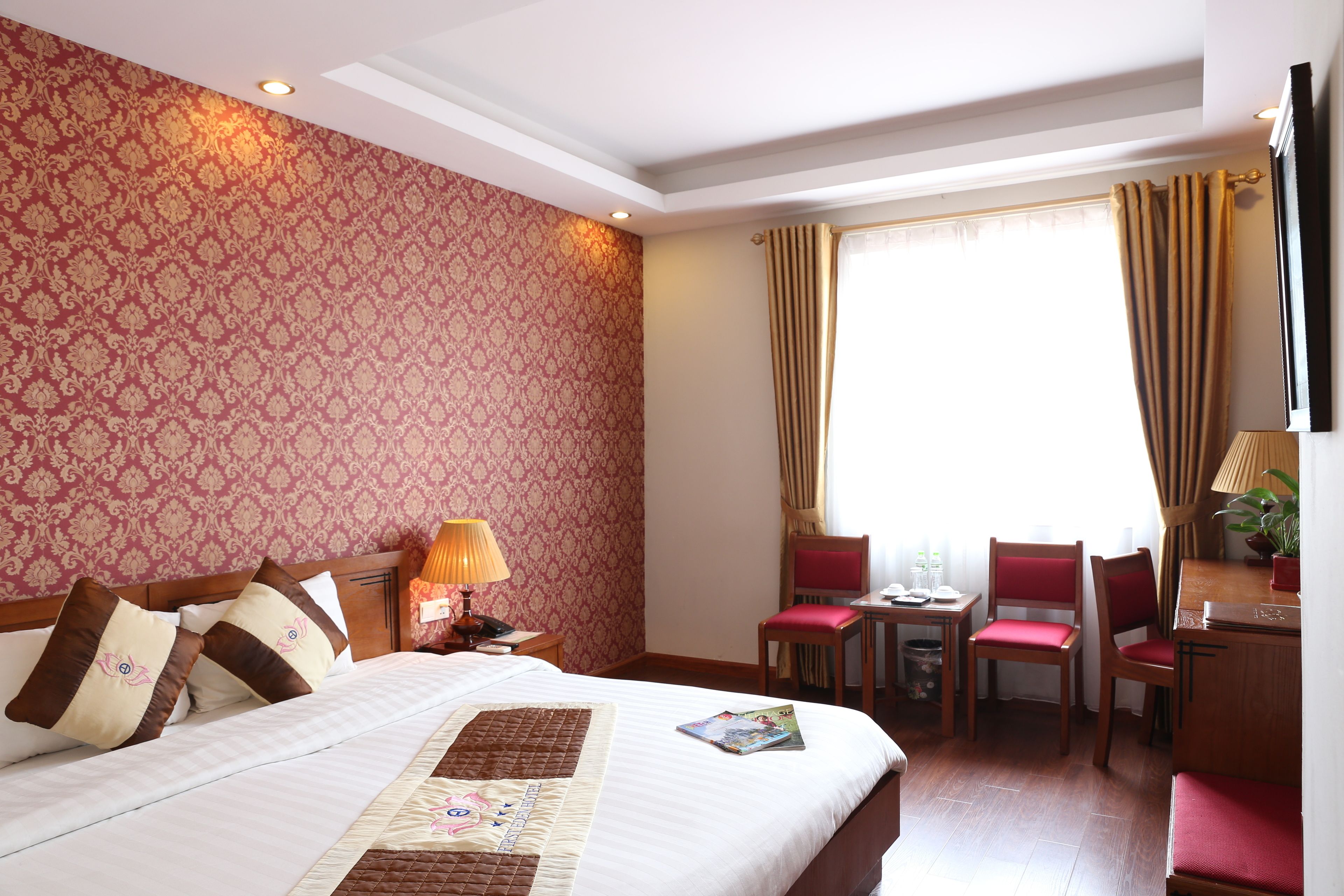 Ein Hotelzimmer mit einem großen Bett, einem Schreibtisch mit Stuhl, einem kleinen Tisch und einem Fenster mit Vorhängen.