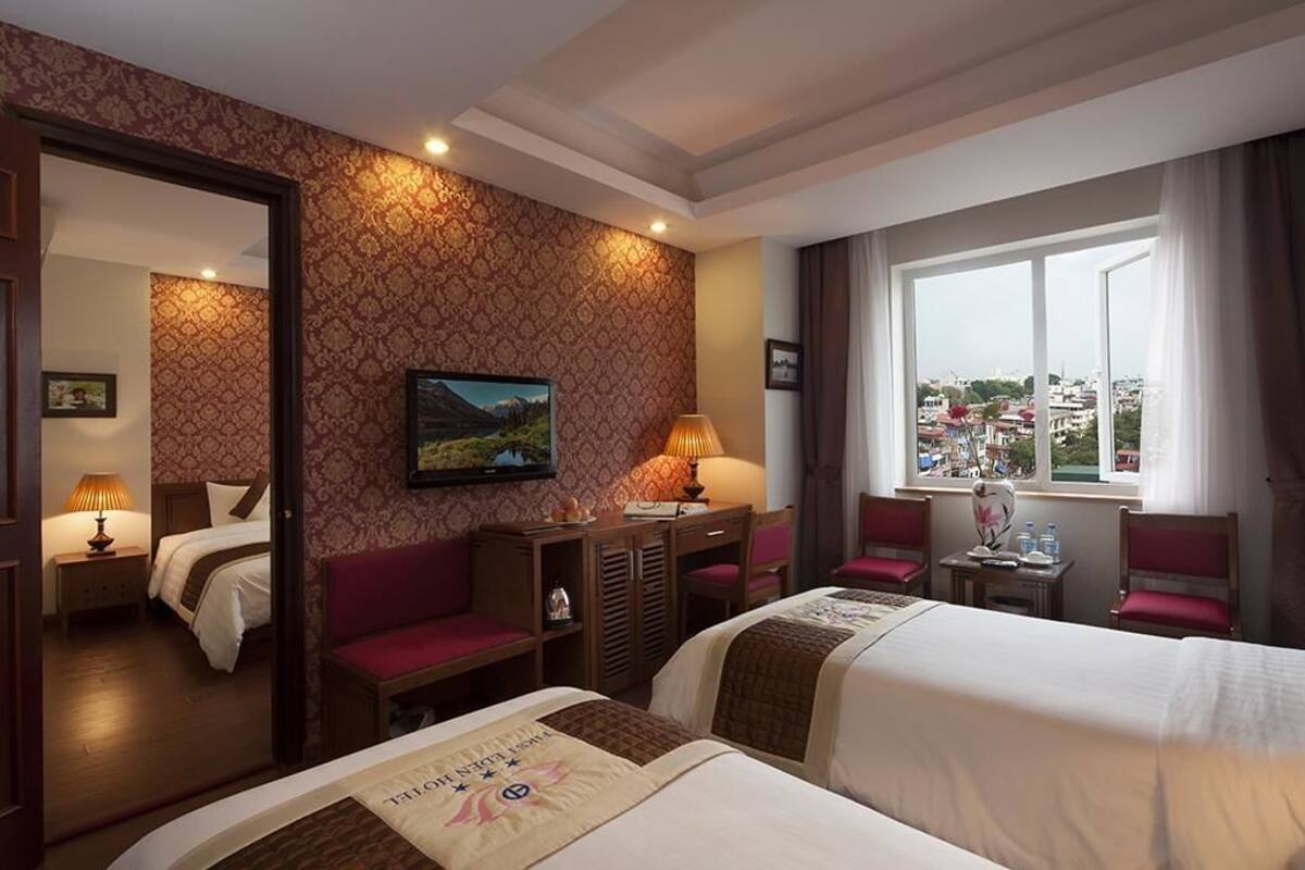 A hotel room with two beds, a desk, a chair, a TV, and a window with a city view.