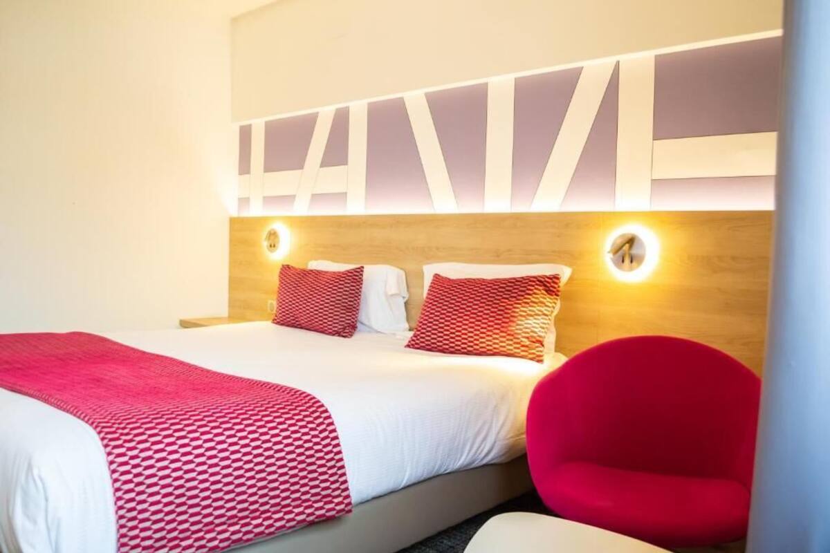 Hotellihuone, jossa on suuri sänky, kaksi yöpöytää ja punainen tuoli.