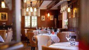 Un restaurant avec des tables rondes disposées pour le service, des murs en bois et des tableaux encadrés qui décorent les murs.