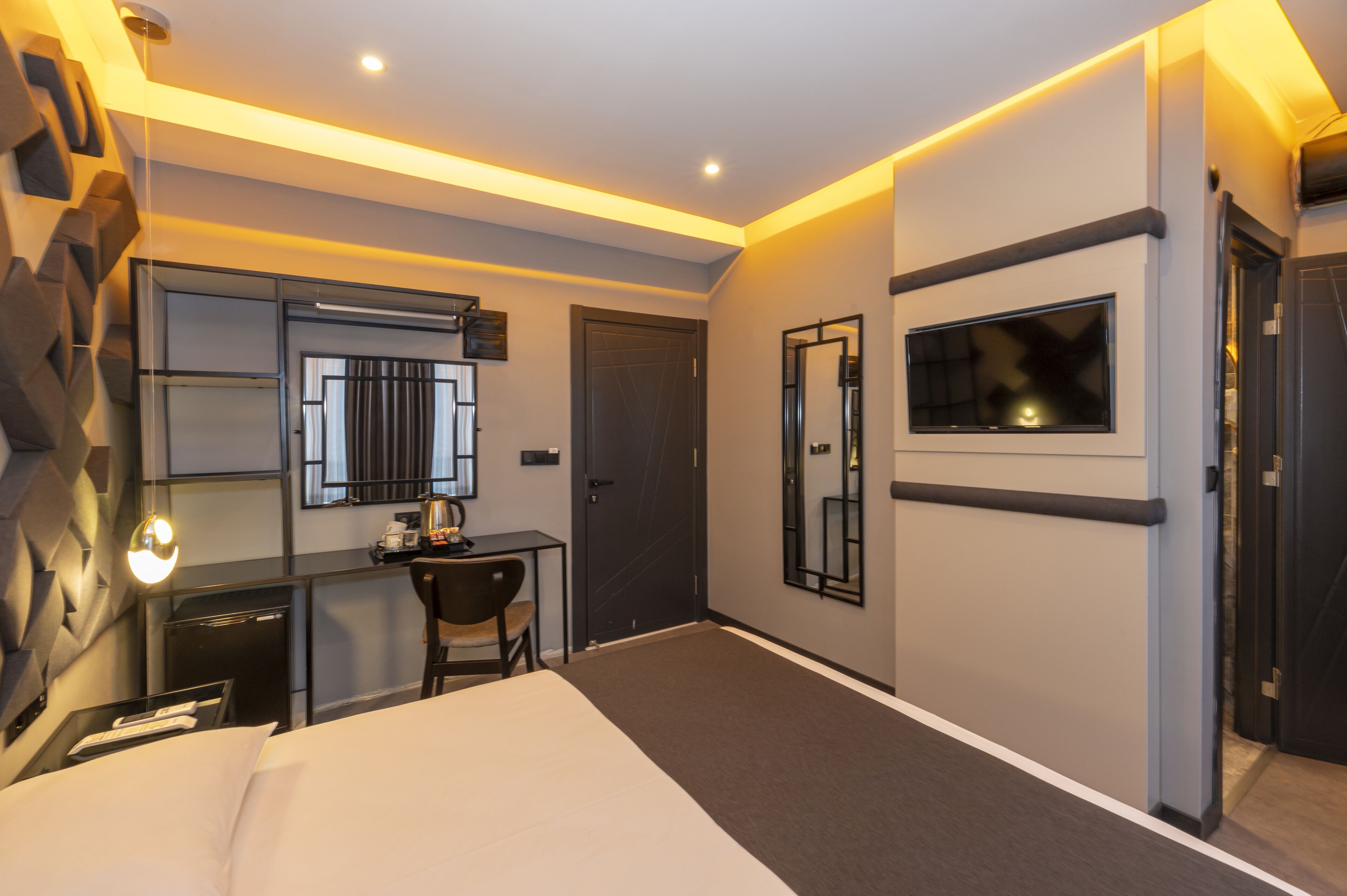 A modern hotel room with a bed, desk, chair, and a TV.