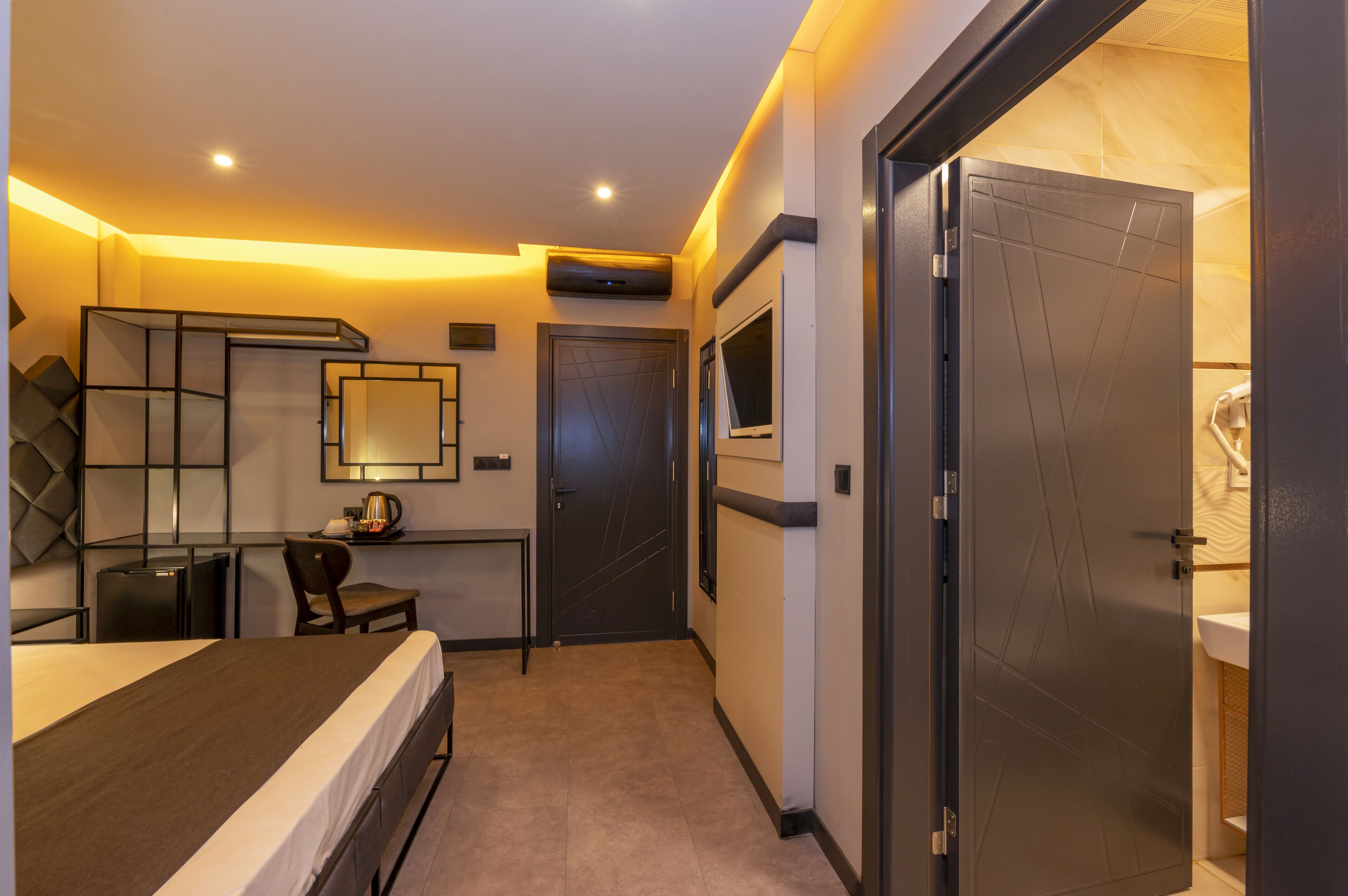 A hotel room with a bed, a desk, a chair, a mirror, and a door leading to a bathroom.