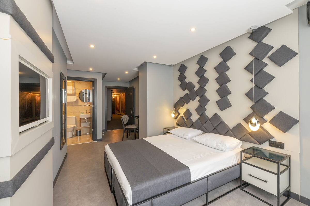 Ein modernes Hotelzimmer mit einem großen Bett, Nachttischen, einem Spiegel und einer Wandleuchte.