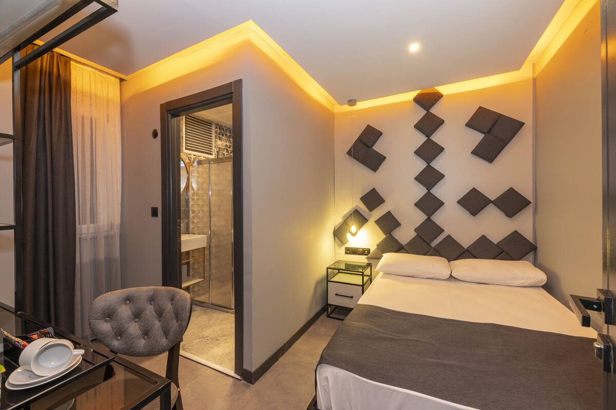Ein modernes Hotelzimmer mit Bett, Schreibtisch mit Stuhl, Nachttisch und einem durchgegangene Tür sichtbaren Badezimmer.