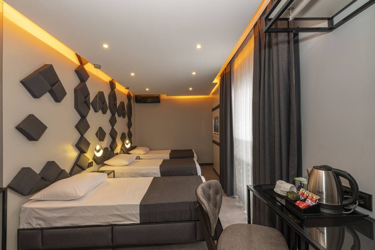 Ein Hotelzimmer mit drei Betten, einem Schreibtisch mit Wasserkocher und einem Stuhl.