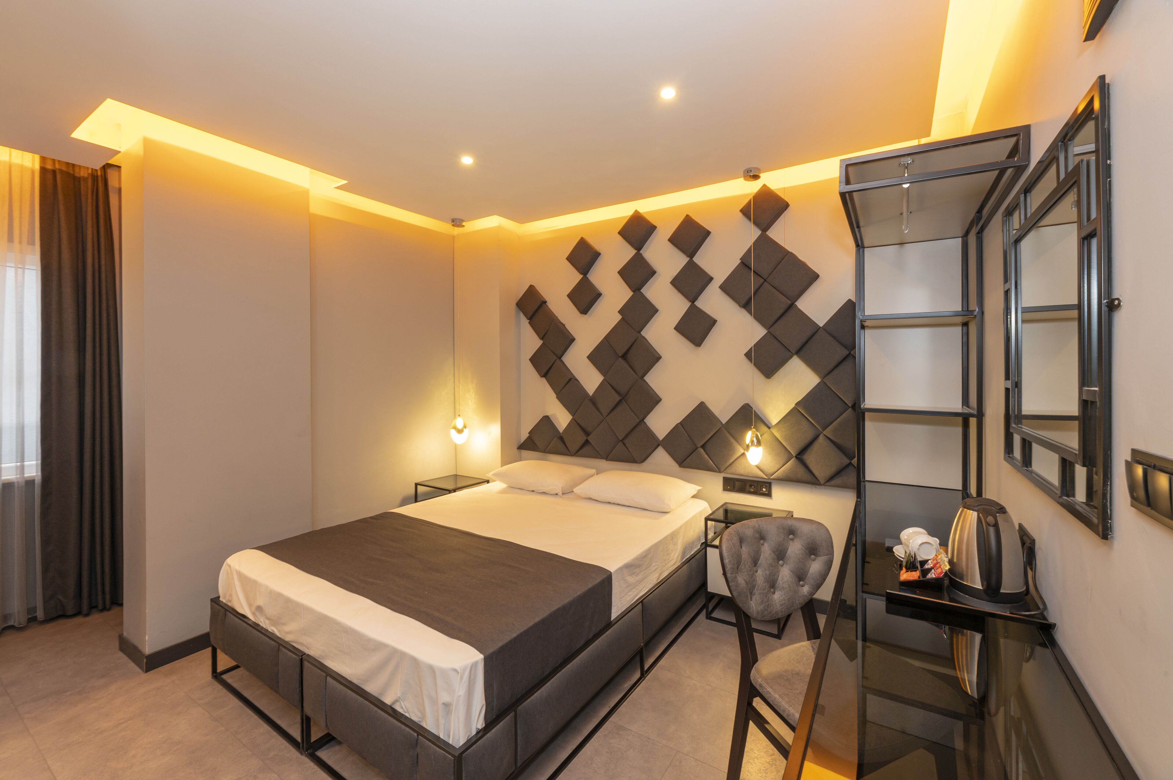 Una habitación de hotel moderna con una cama grande, mesitas de noche, una silla y un escritorio con tetera.