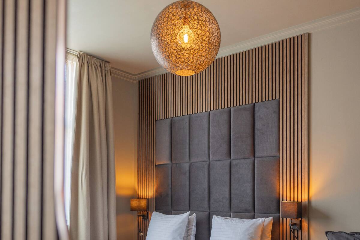 Una habitación de hotel moderna con una cama grande, una lámpara colgante redonda y un cabecero de madera.