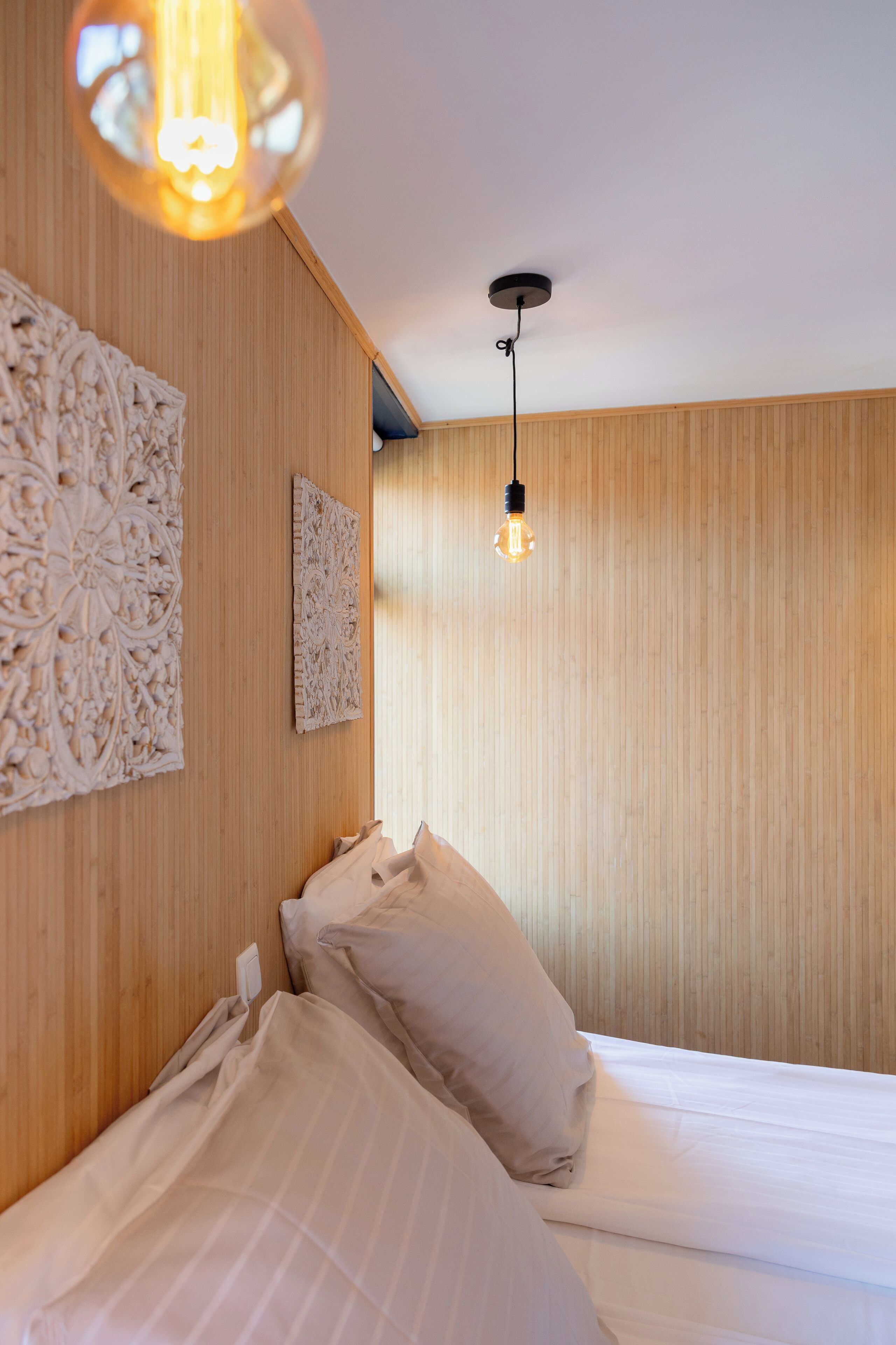 A bedroom with a wooden wall, a bed with white linens, and a hanging light fixture.