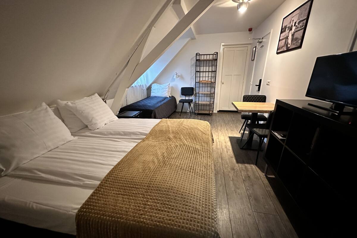 Un dormitorio con cama, una mesita, televisor y una silla.