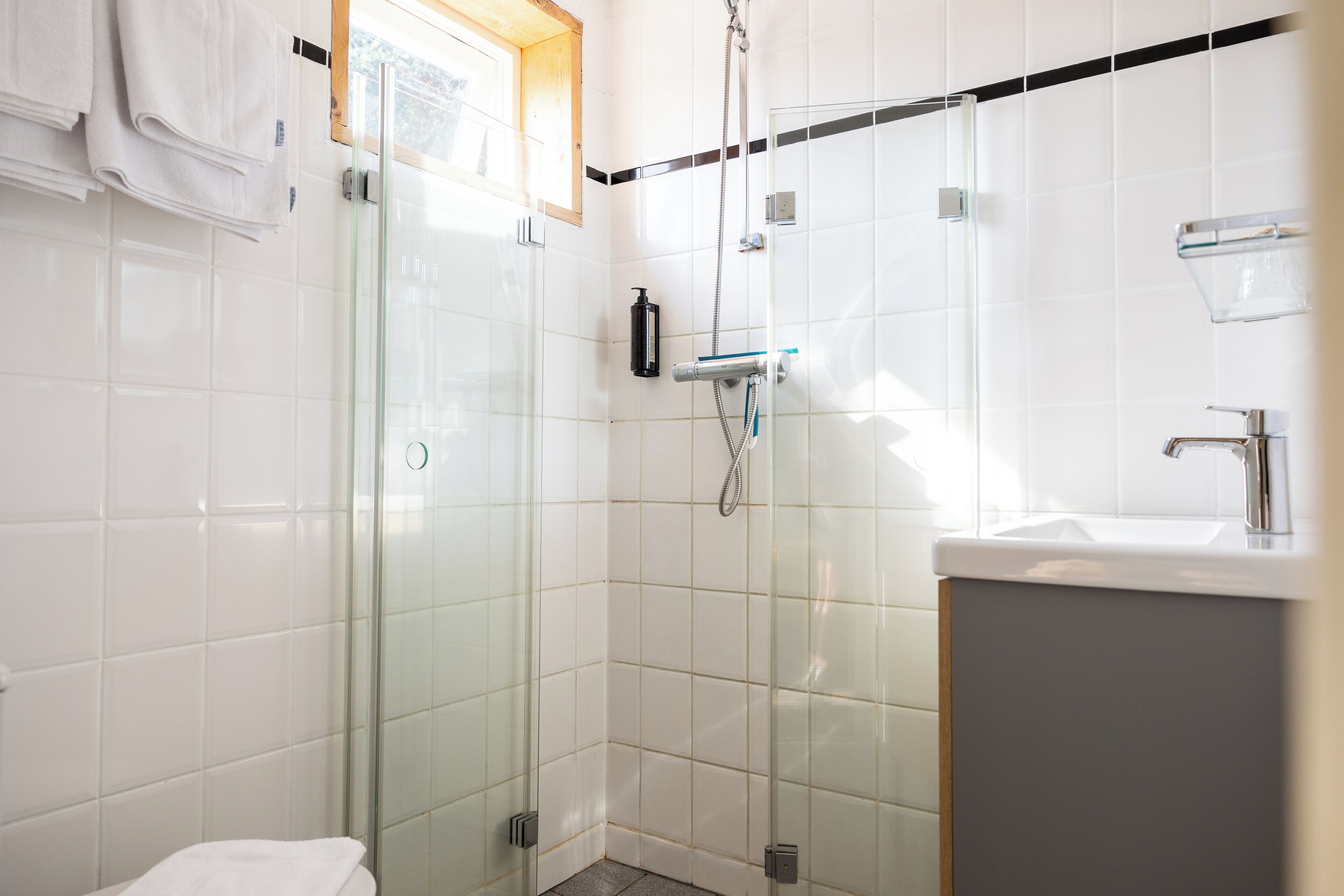 A modern bathroom with a glass-enclosed shower, a white sink, and a towel rack.