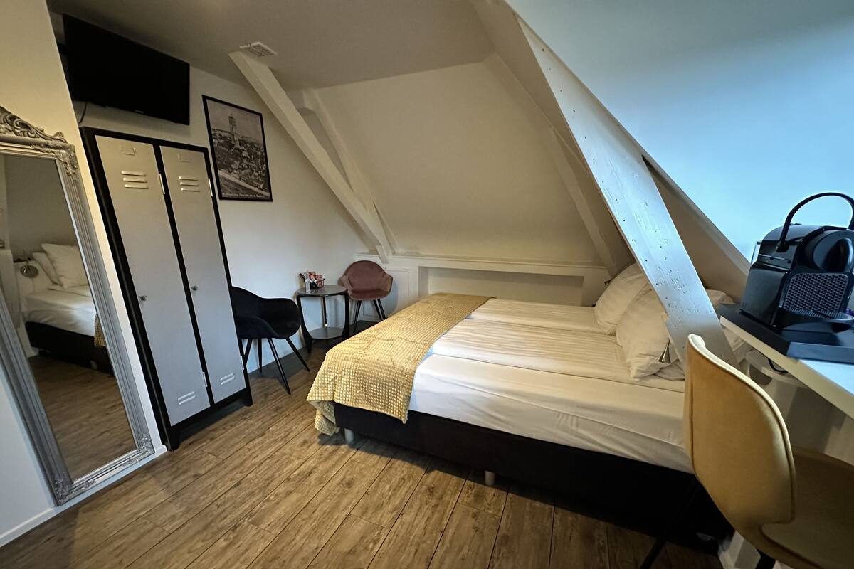Un dormitorio con cama, escritorio, silla, espejo y armario.