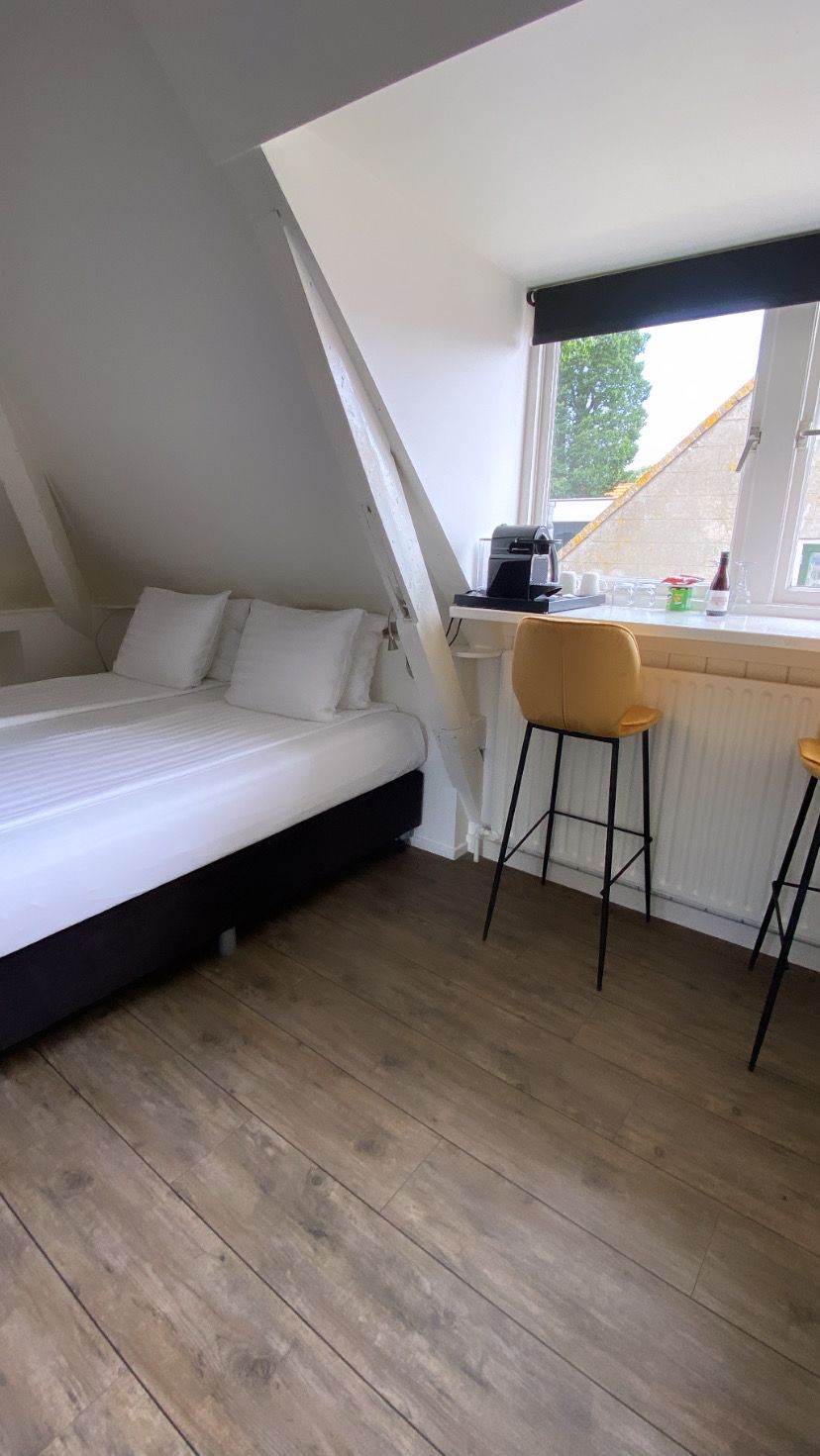 Un dormitorio con techo inclinado, una cama, un escritorio con silla y una ventana.
