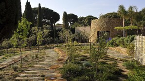 A garden with stone pathways, various plants, and a stone building. - MUSE Saint Tropez (Ramatuelle)