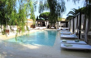 A pool area with lounge chairs and umbrellas, surrounded by trees and a building in the background. - MUSE Saint Tropez (Ramatuelle)