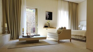 A modern hotel room with a large bed, a sofa, a small table with a chessboard, and a view of a stone wall outside. - MUSE Saint Tropez (Ramatuelle)