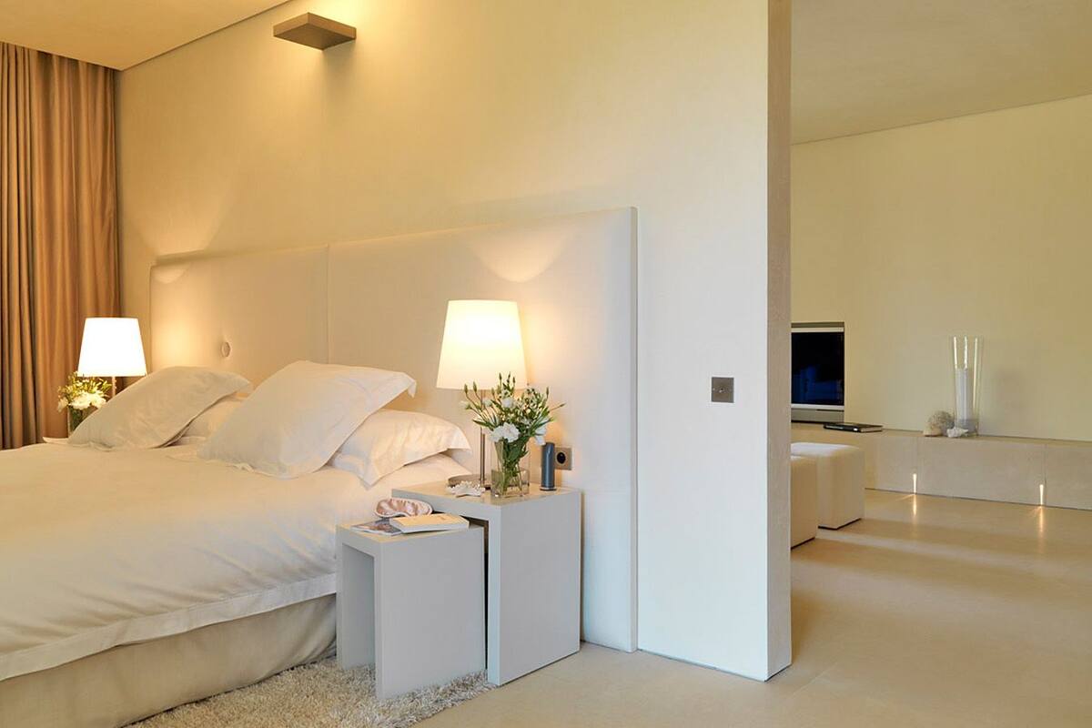 A modern hotel room with a large bed, bedside tables, a nightstand with a lamp, a mirror, and a TV.