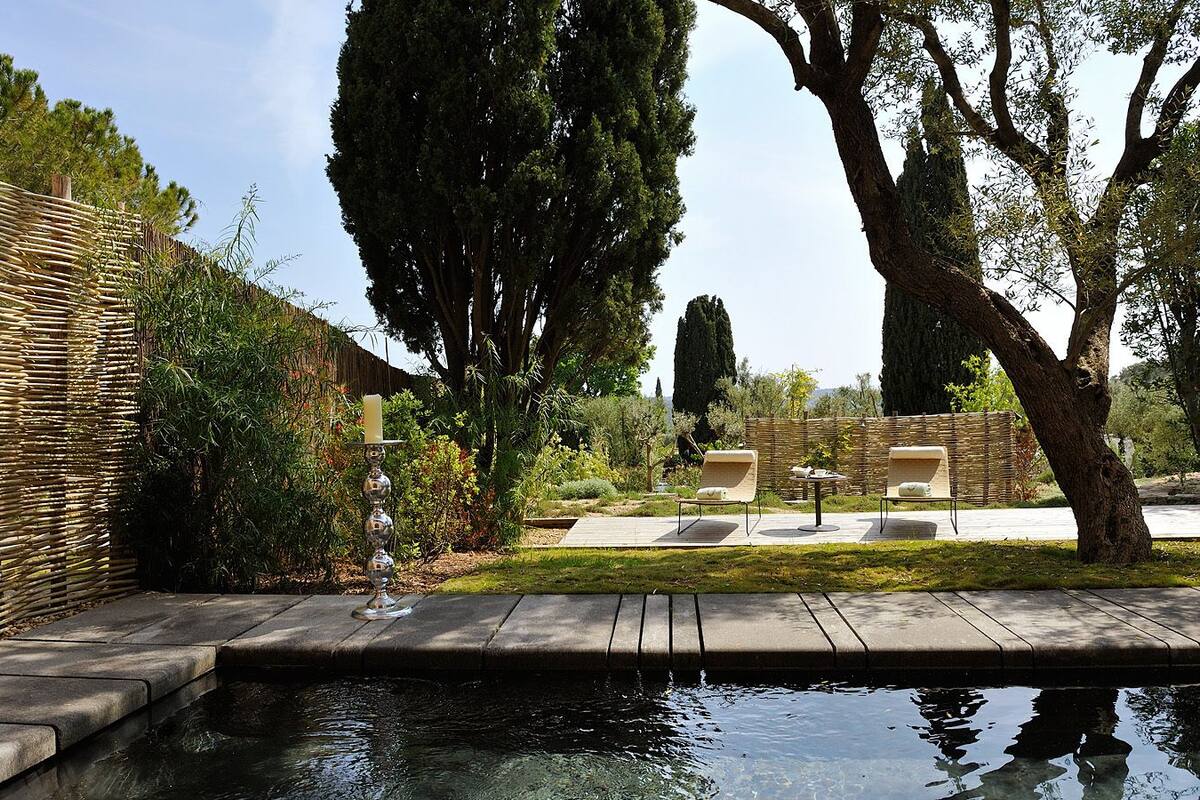 A serene garden with a pool, a wicker fence, and outdoor seating.