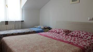 Ein Schlafzimmer mit zwei Betten, einem Fenster mit Vorhängen, einem Bild an der Wand und einem Lichtschalter.