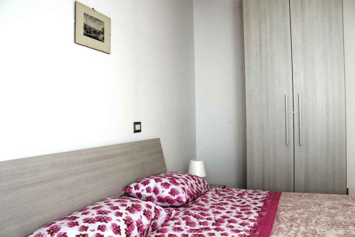 A bedroom with a bed, a wardrobe, and a wall-mounted picture.