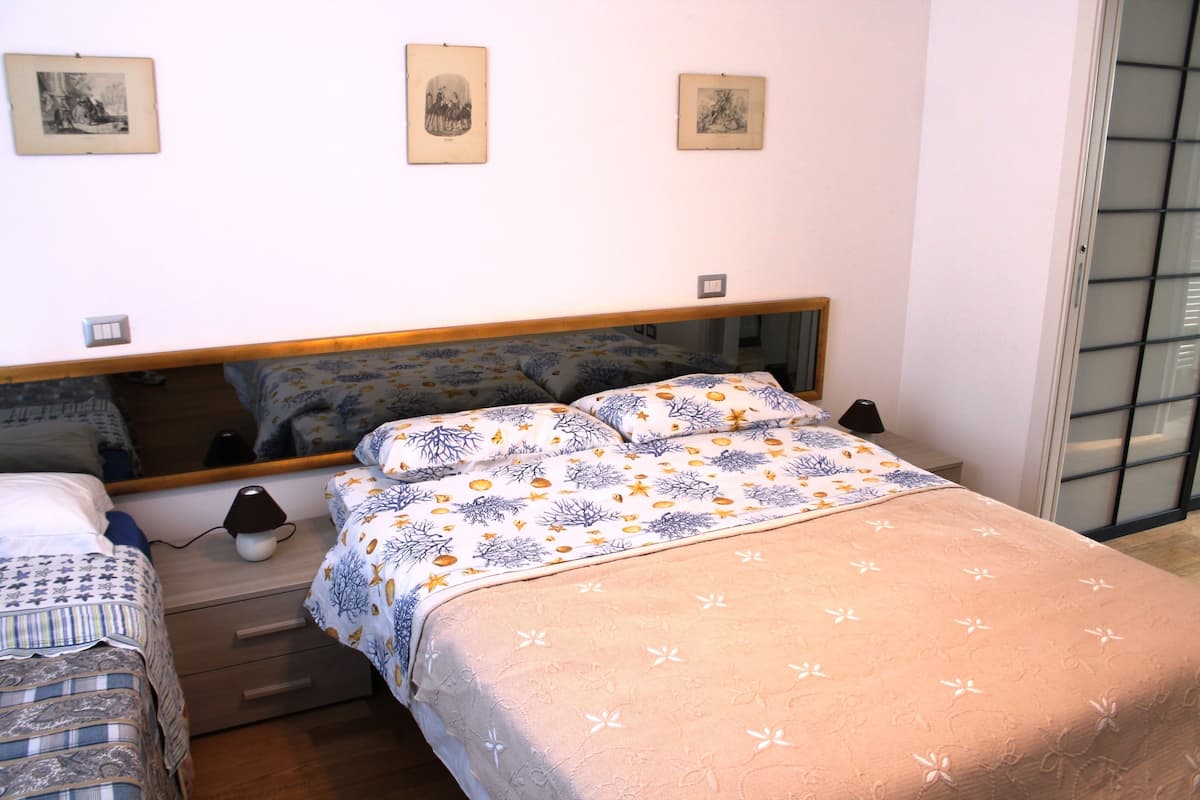 A bedroom with a bed, a bedside table, a lamp, and a mirror on the wall.
