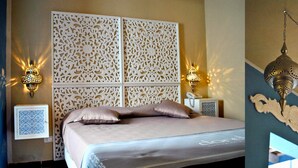 Habitación de hotel con cama, paneles decorativos en la pared, dos lámparas fijadas a la pared y una lámpara colgante.