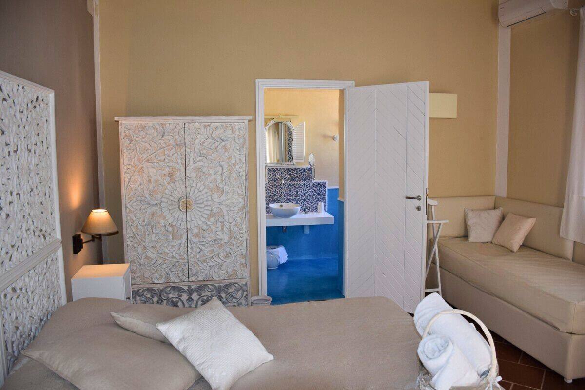 A bedroom with a bed, a wardrobe, a bathroom visible through an open door, and a sofa.