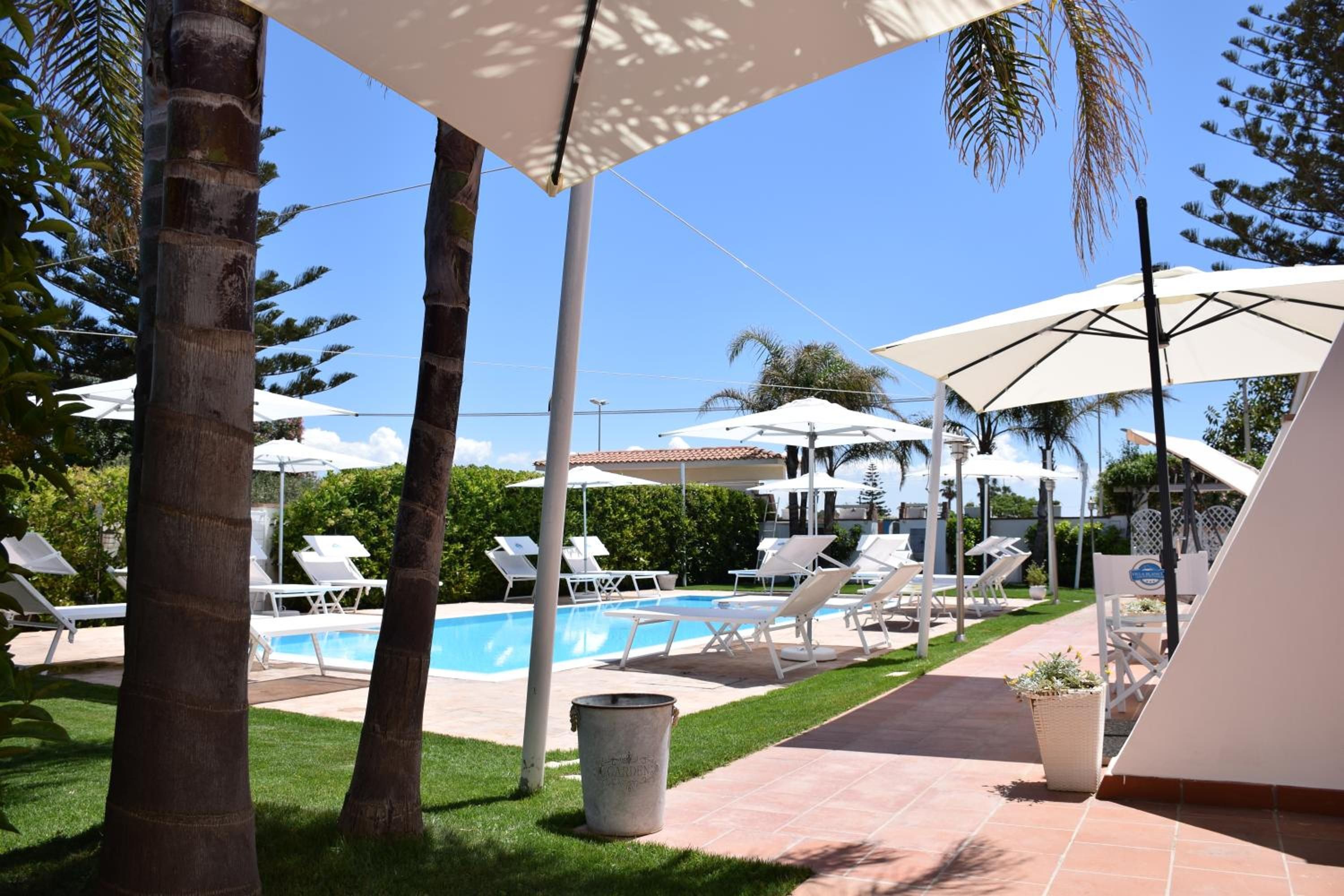 Ein Poolbereich mit Liegestühlen und Sonnenschirmen, umgeben von Palmen und blauem Himmel.