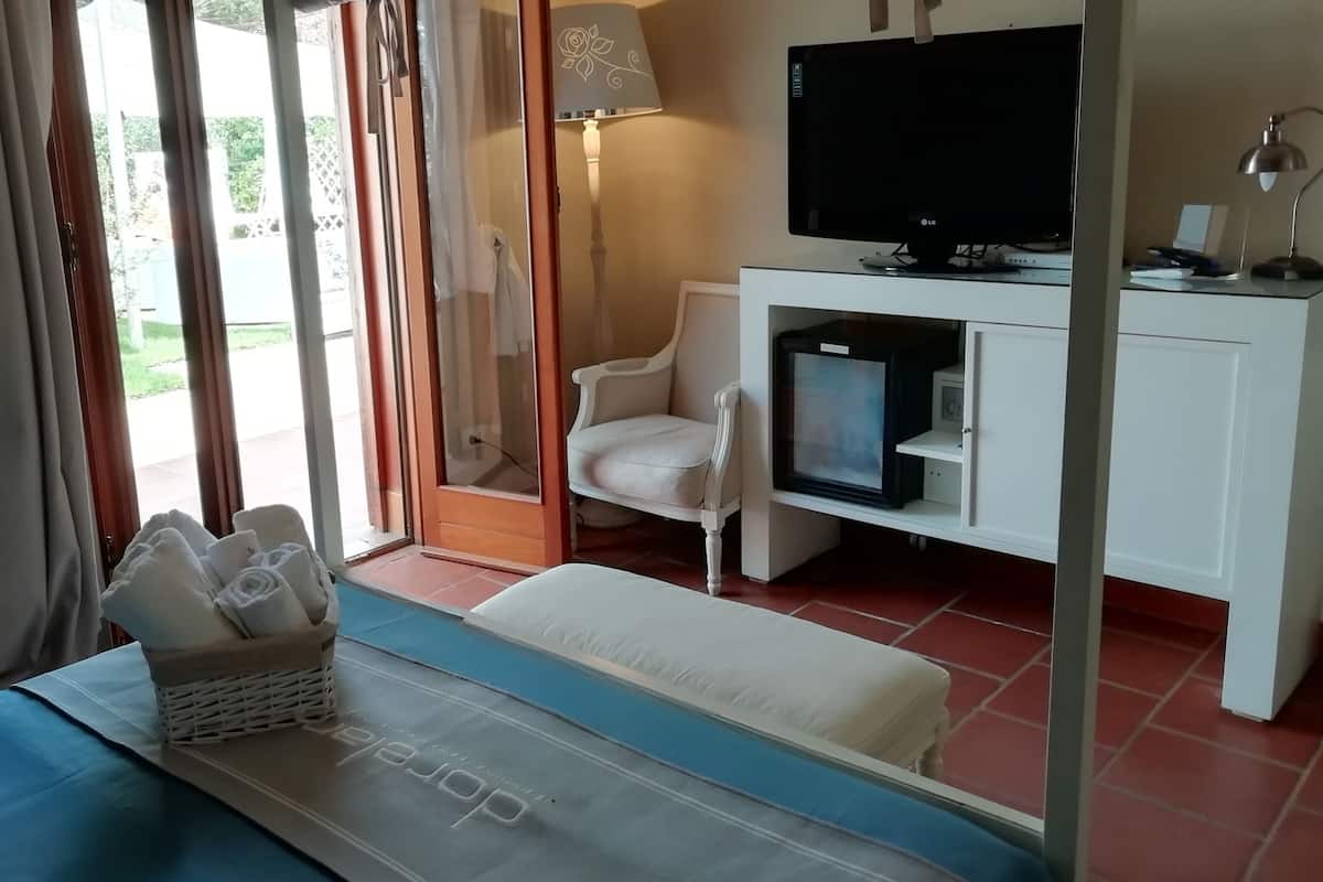 A hotel room with a bed, a desk with a TV, a lamp, and a window with curtains.