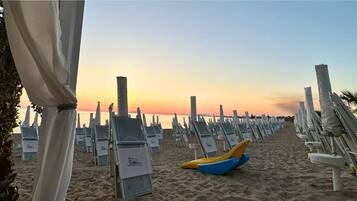 Una spiaggia con file di lettini e una barca gialla e blu sulla sabbia.