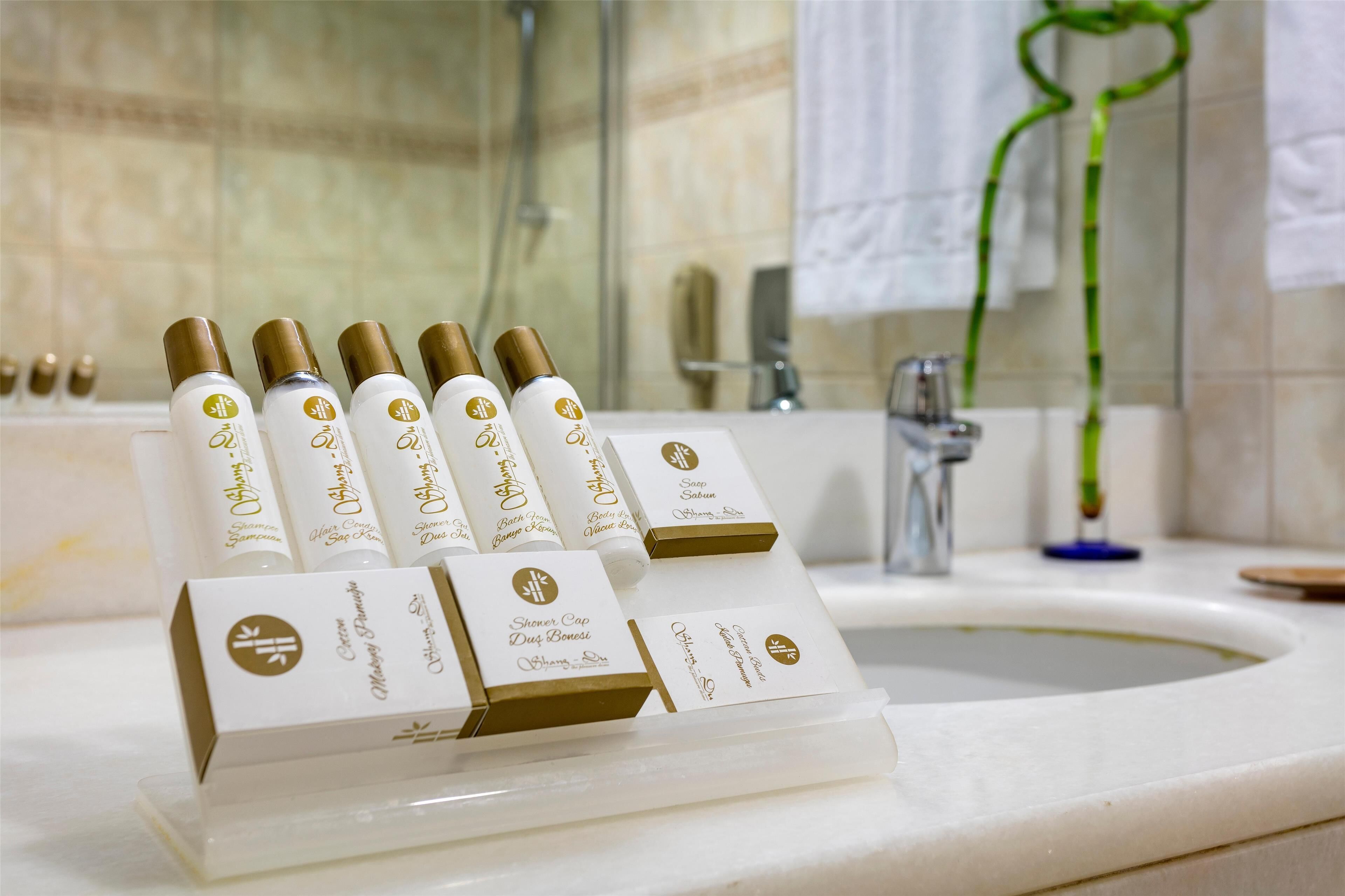 Baño con lavamanos, espejo y ducha. En la encimera hay botellas de champú y acondicionador.