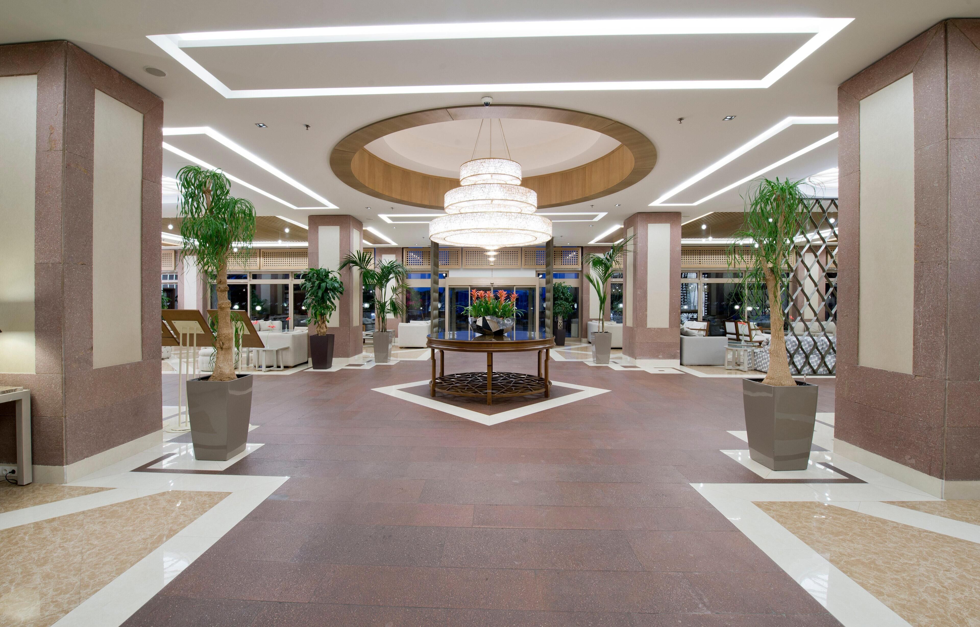 Un hall d’entrée spacieux agrémenté d’une table décorative centrale, de plantes en pot et d’un lustre moderne.