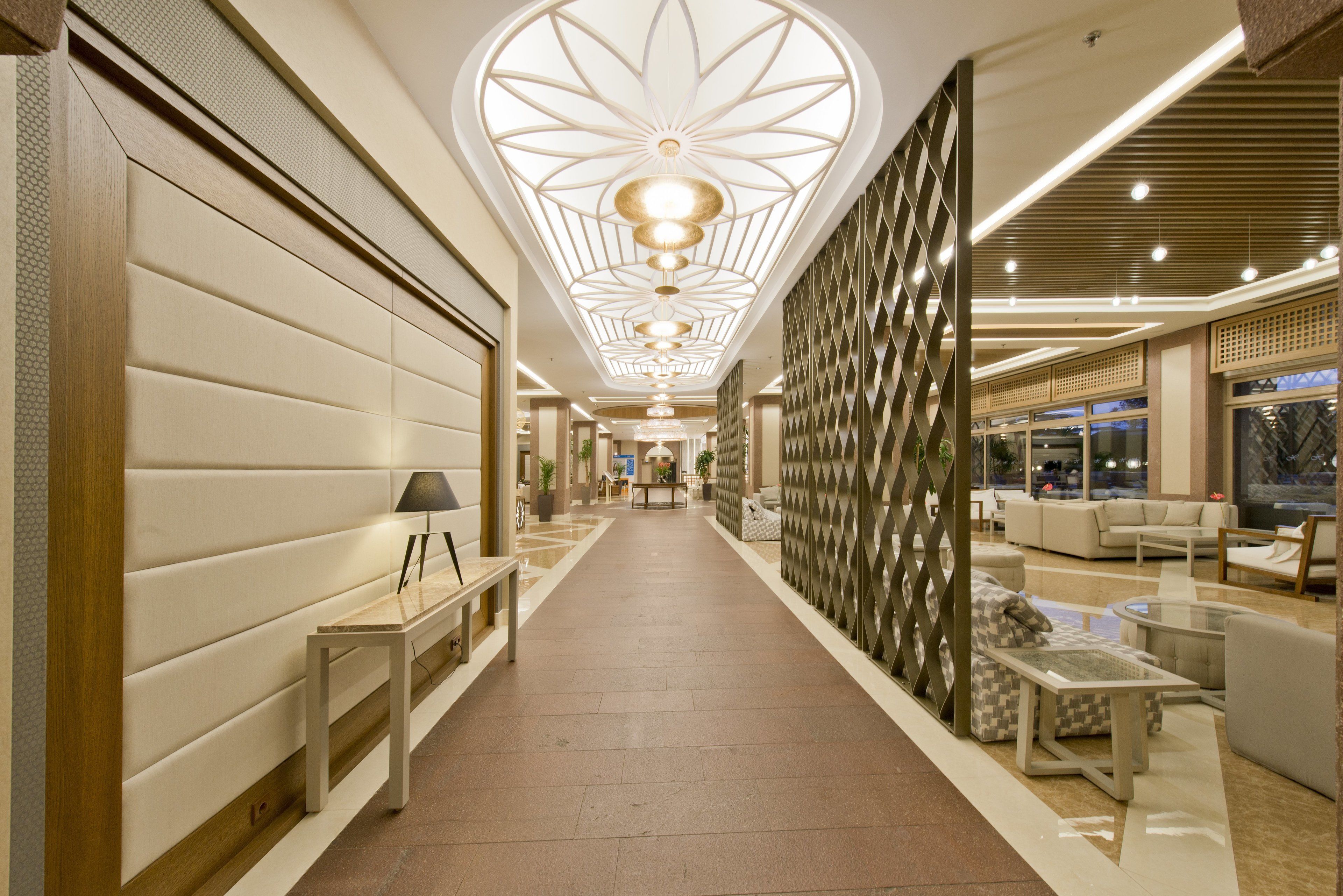 Un couloir d’hôtel moderne, avec une allée centrale, des espaces de détente et un plafond décoratif.