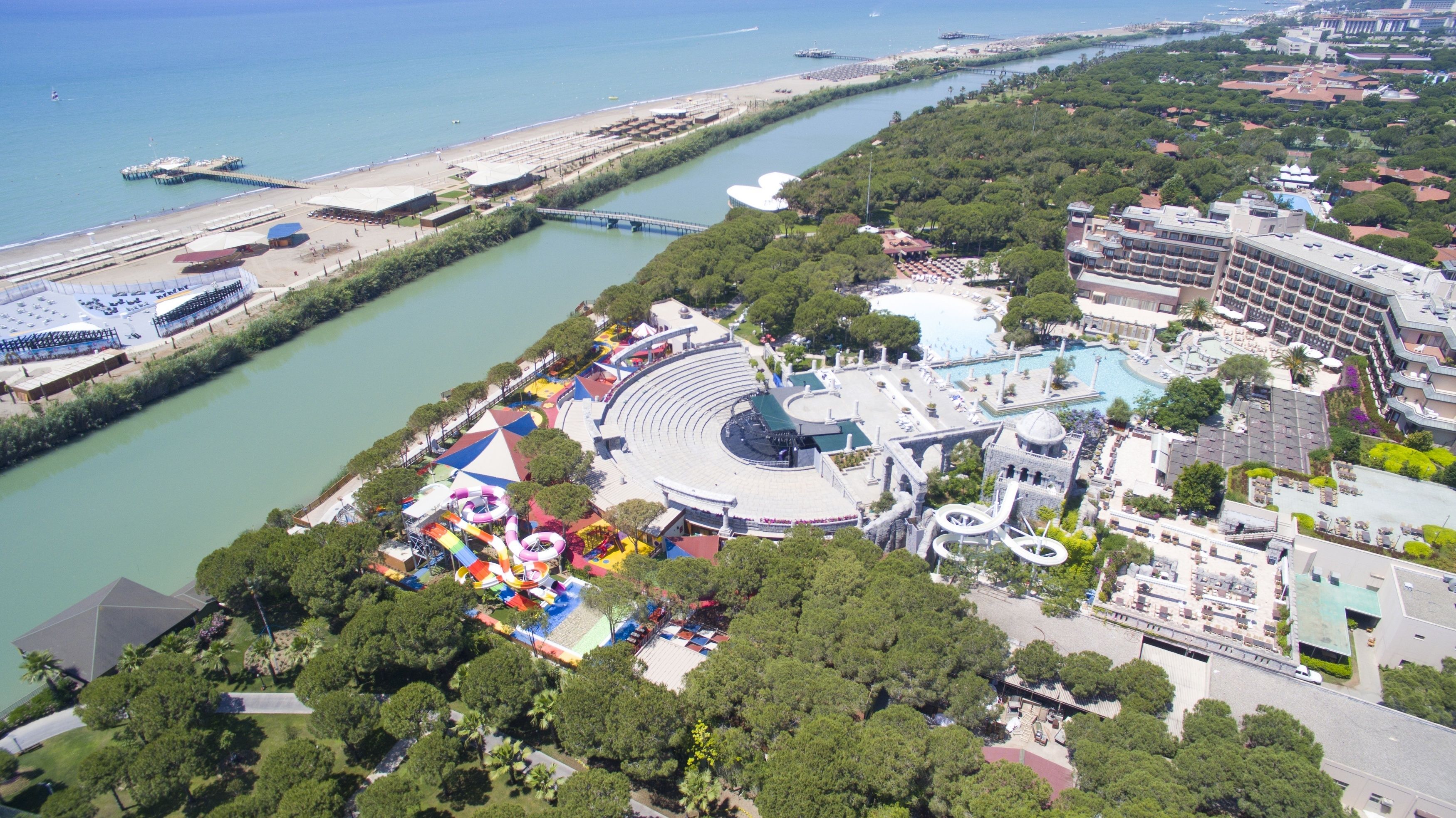An aerial view of a coastal resort with a large amphitheater, a water park, and a marina.